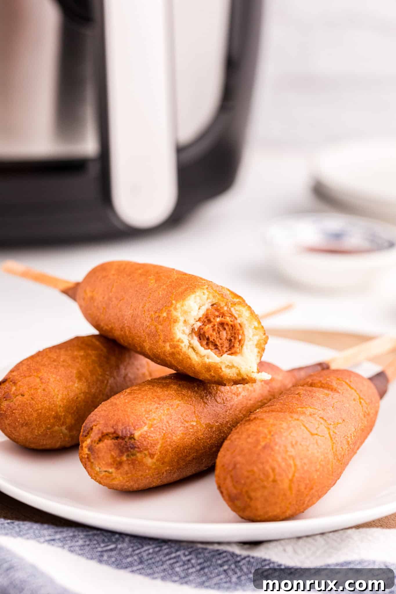 Close-up of air fryer corn dogs on a plate, one with a bite taken, showing the crispy texture.