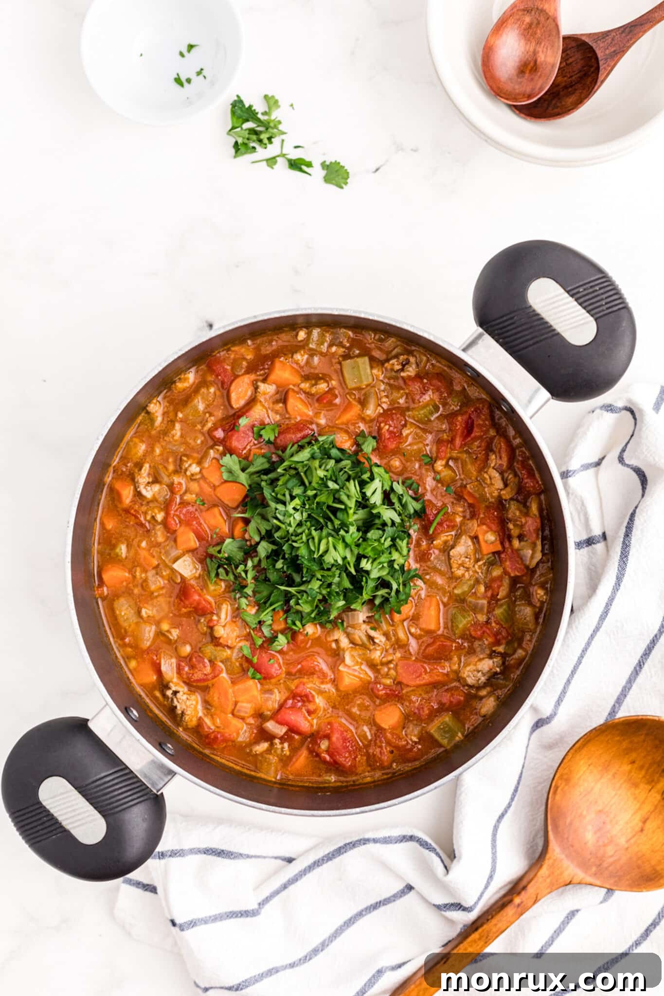 Freshly chopped parsley being stirred into the steaming ground turkey lentil soup, adding a vibrant finish.