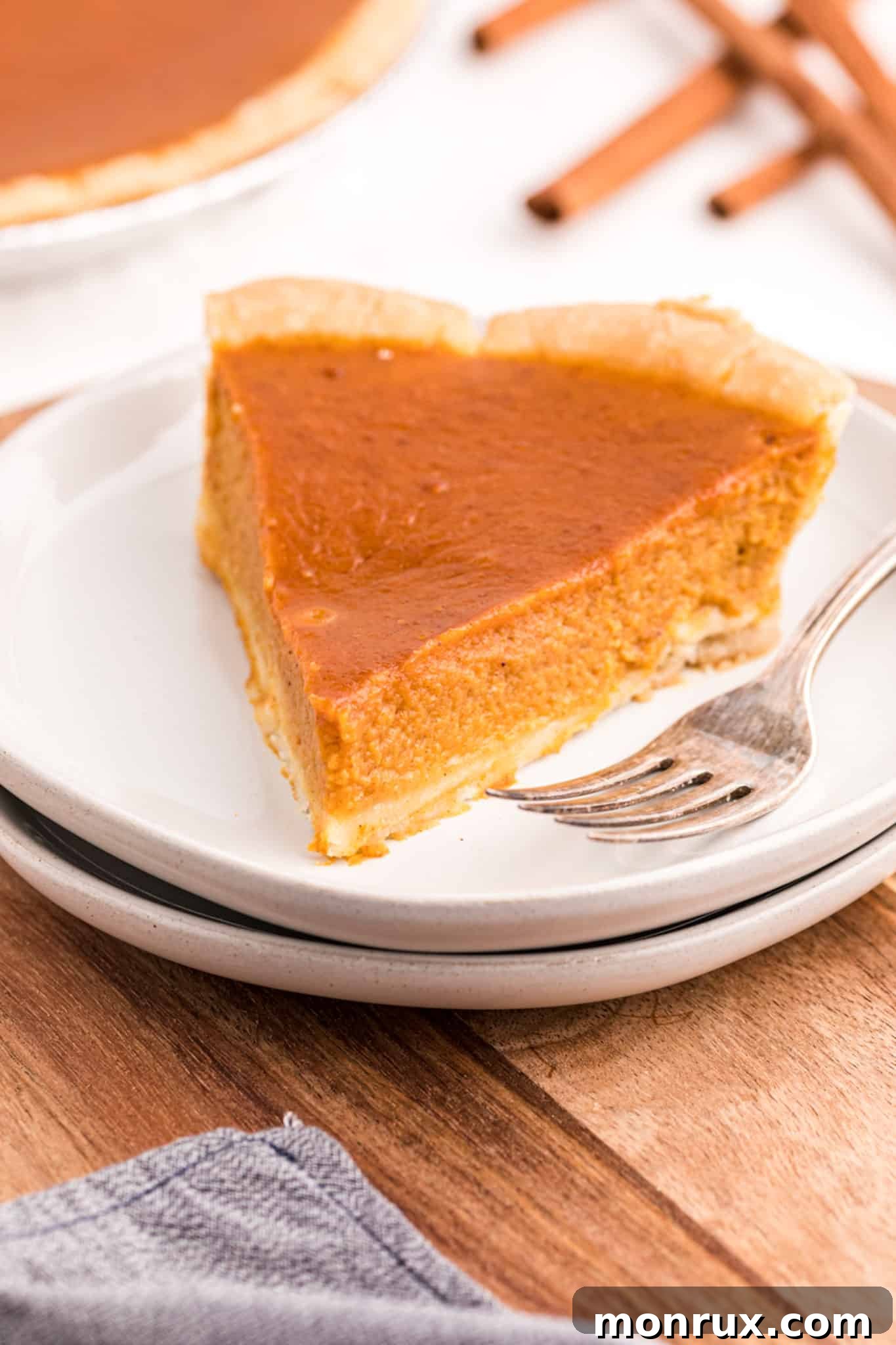 A beautifully presented slice of golden-brown gluten-free and dairy-free pumpkin pie on a pristine white plate, garnished with a sprinkle of cinnamon, ready to be enjoyed.