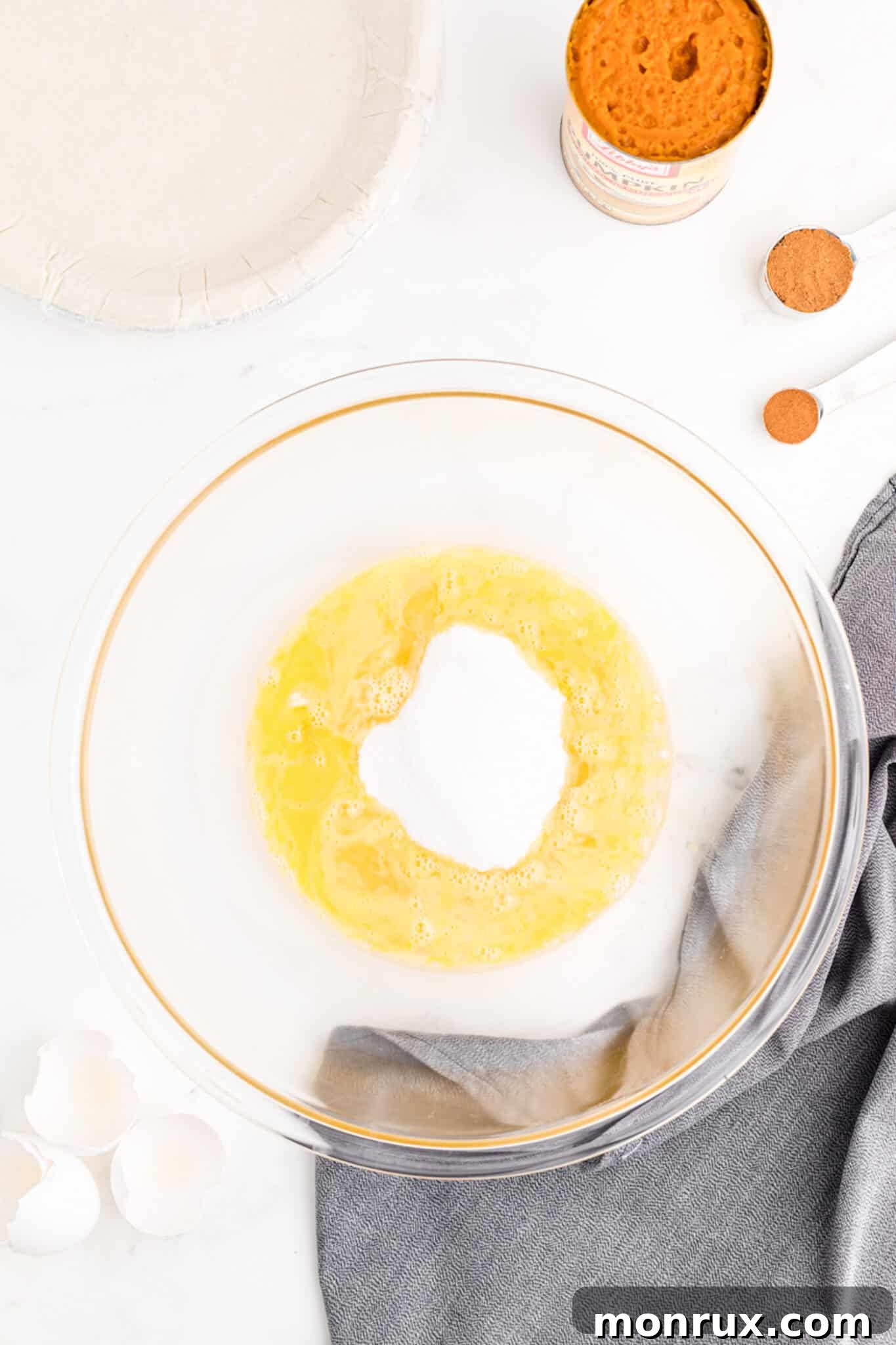 A mixing bowl containing granulated sugar and two lightly beaten eggs, demonstrating the first step of combining wet and dry ingredients.