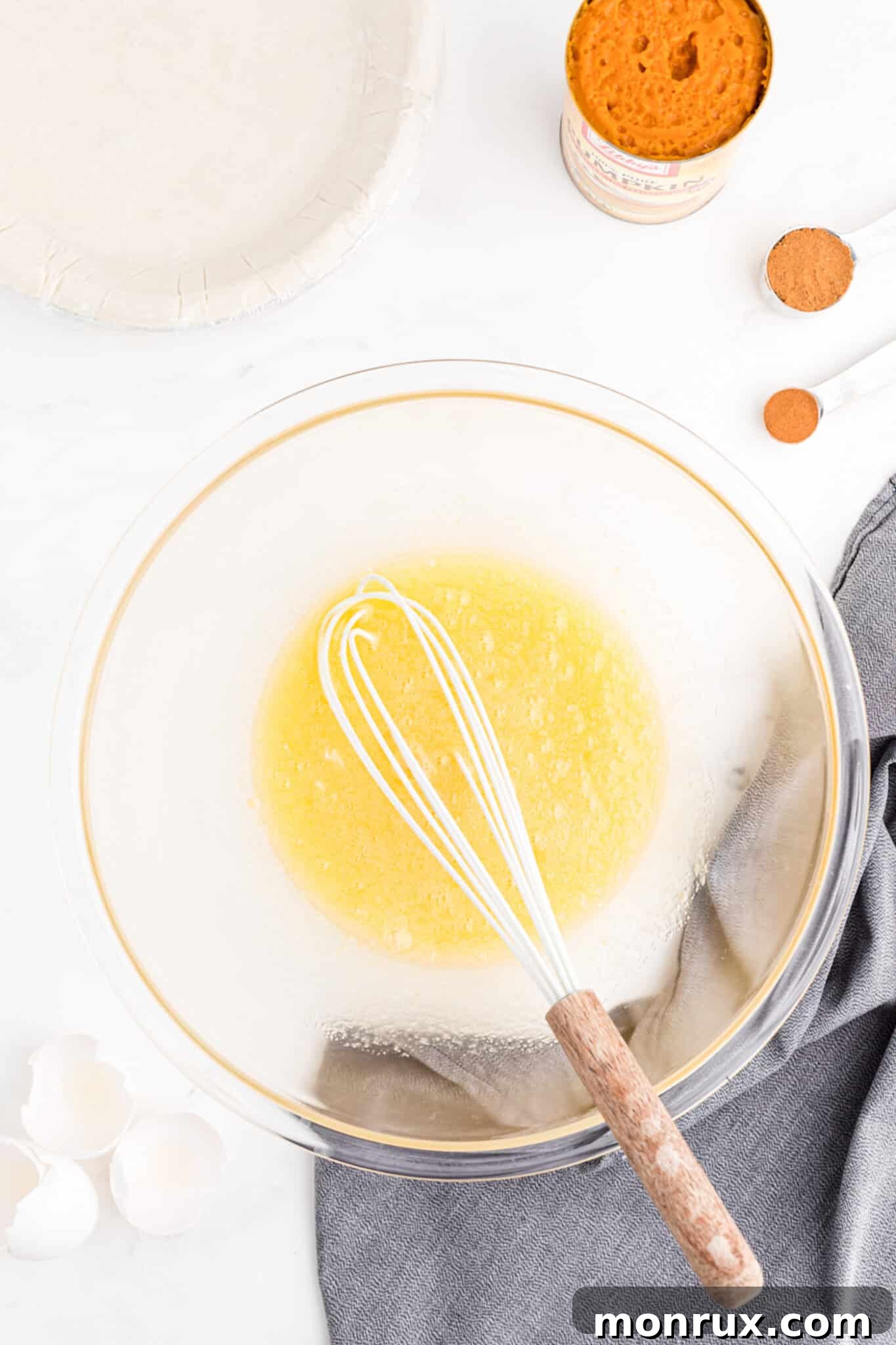 A close-up shot of a whisk actively combining sugar and eggs in a mixing bowl until light and foamy.
