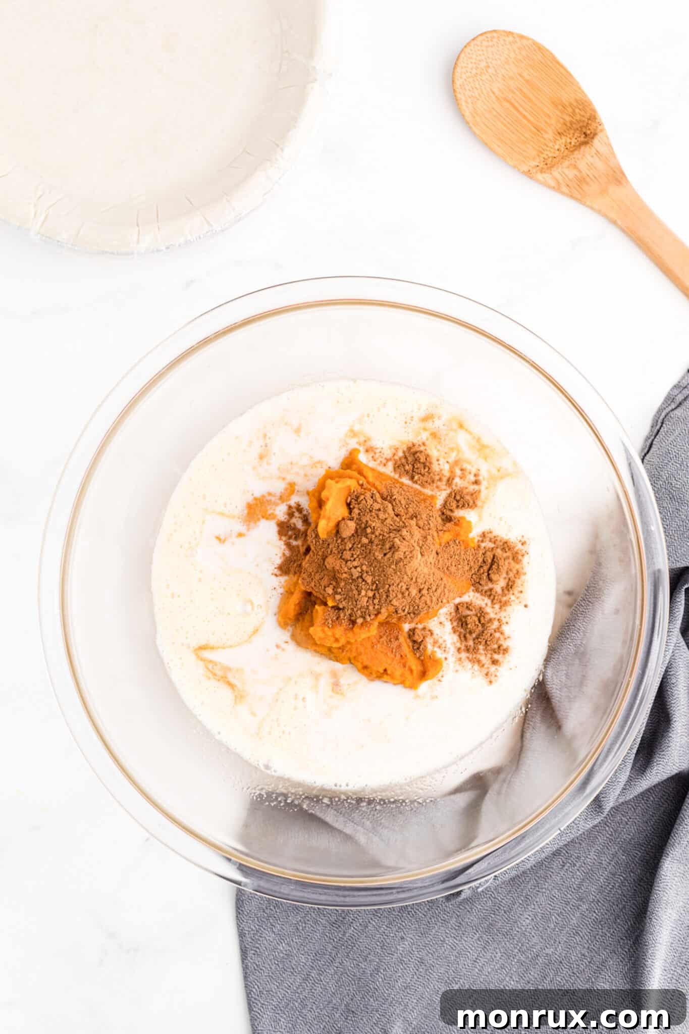 A large mixing bowl filled with all the creamy, spiced ingredients for the dairy-free pumpkin pie filling, including pumpkin puree, coconut milk, and spices, before final mixing.