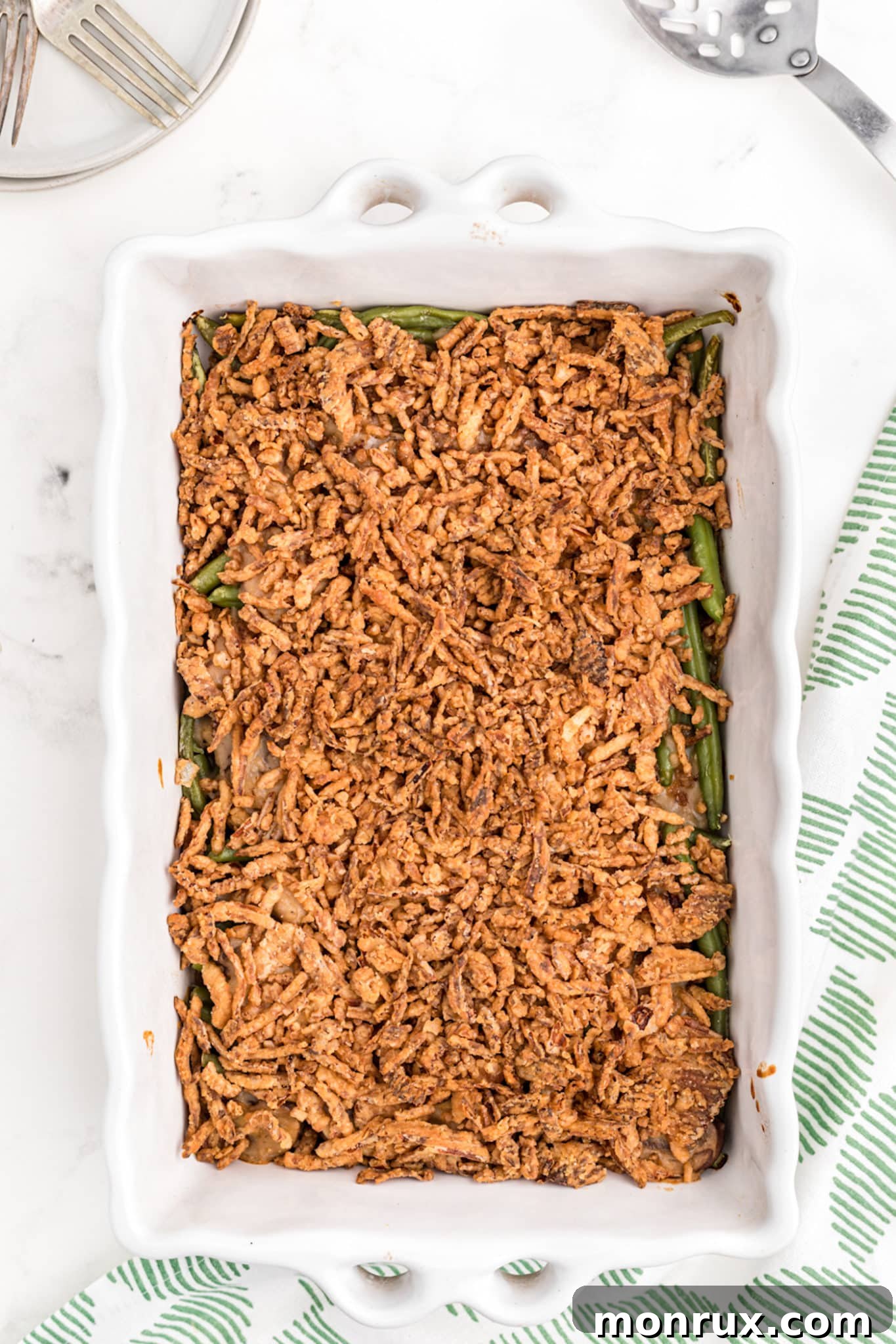 A beautifully baked dairy-free green bean casserole, golden brown and bubbly, in a white baking dish, ready to be served at a holiday feast.
