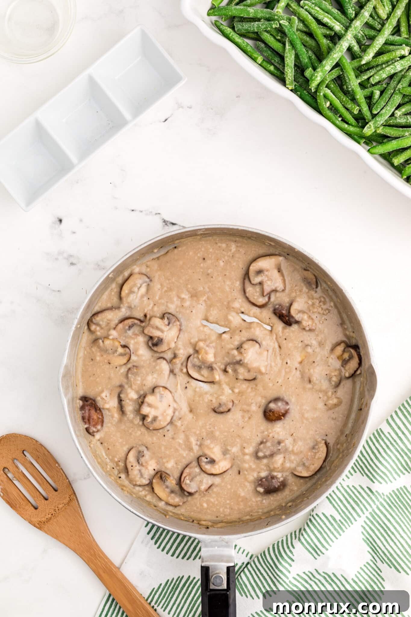 Adding gluten-free flour to sautéed mushrooms in a pan, stirring to create a dairy-free roux for the casserole sauce.