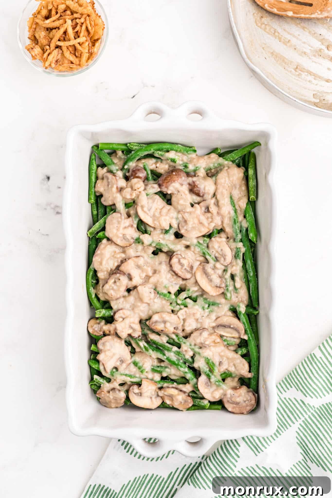 Pouring the creamy dairy-free mushroom sauce over a bed of green beans in a casserole dish, preparing it for baking.