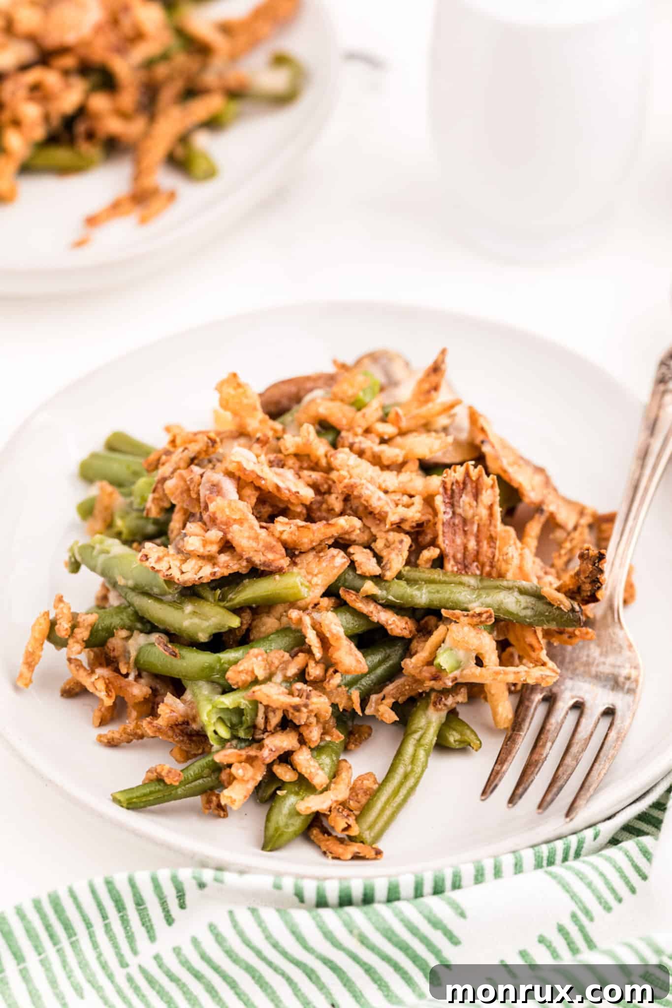 Two individual servings of dairy-free green bean casserole, showing the creamy texture and crispy onion topping, plated on a dark surface.
