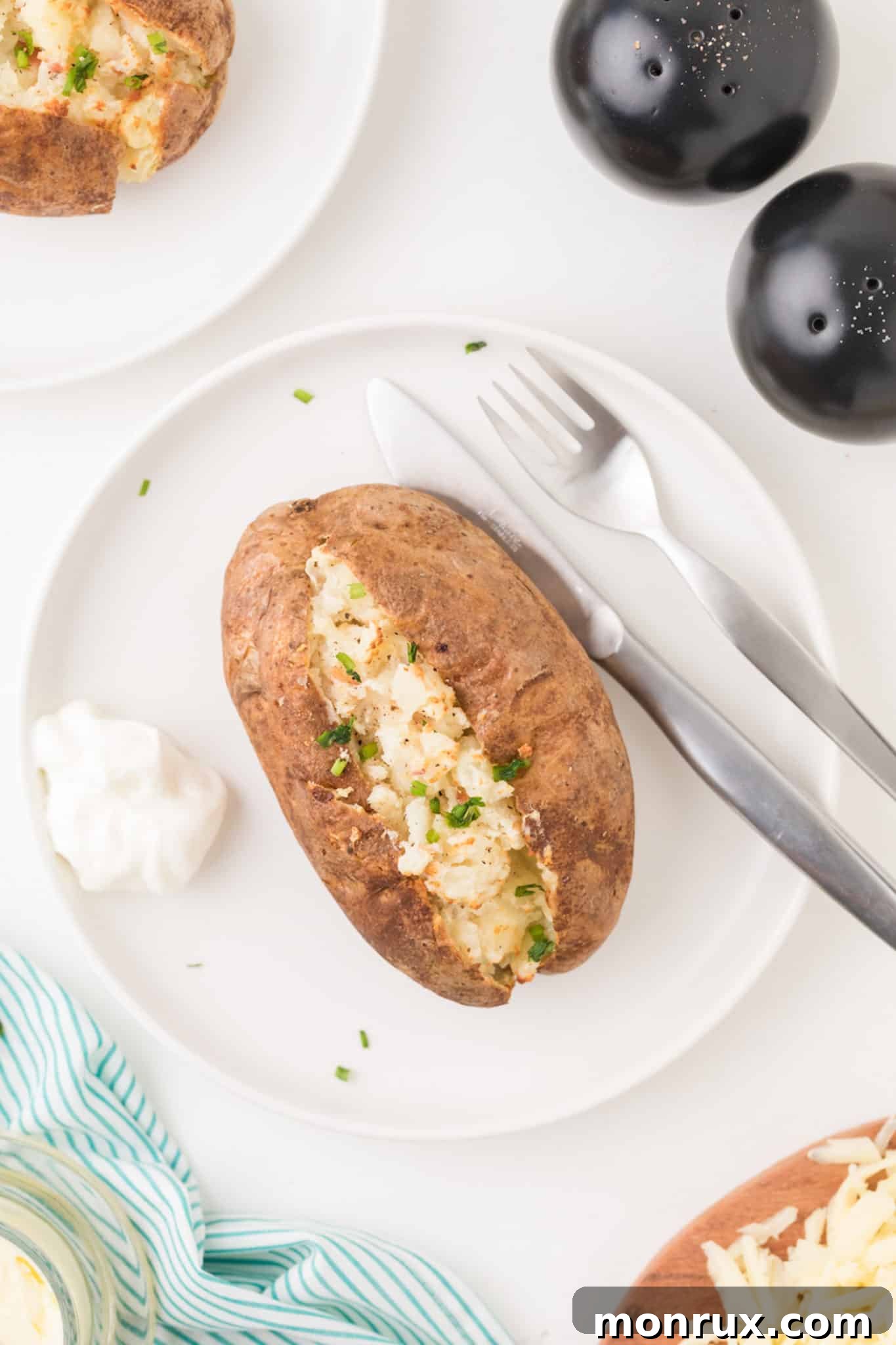 A perfectly golden brown and creamy air fryer twice baked potato, garnished with fresh chives, served on a crisp white plate, ready to be enjoyed.