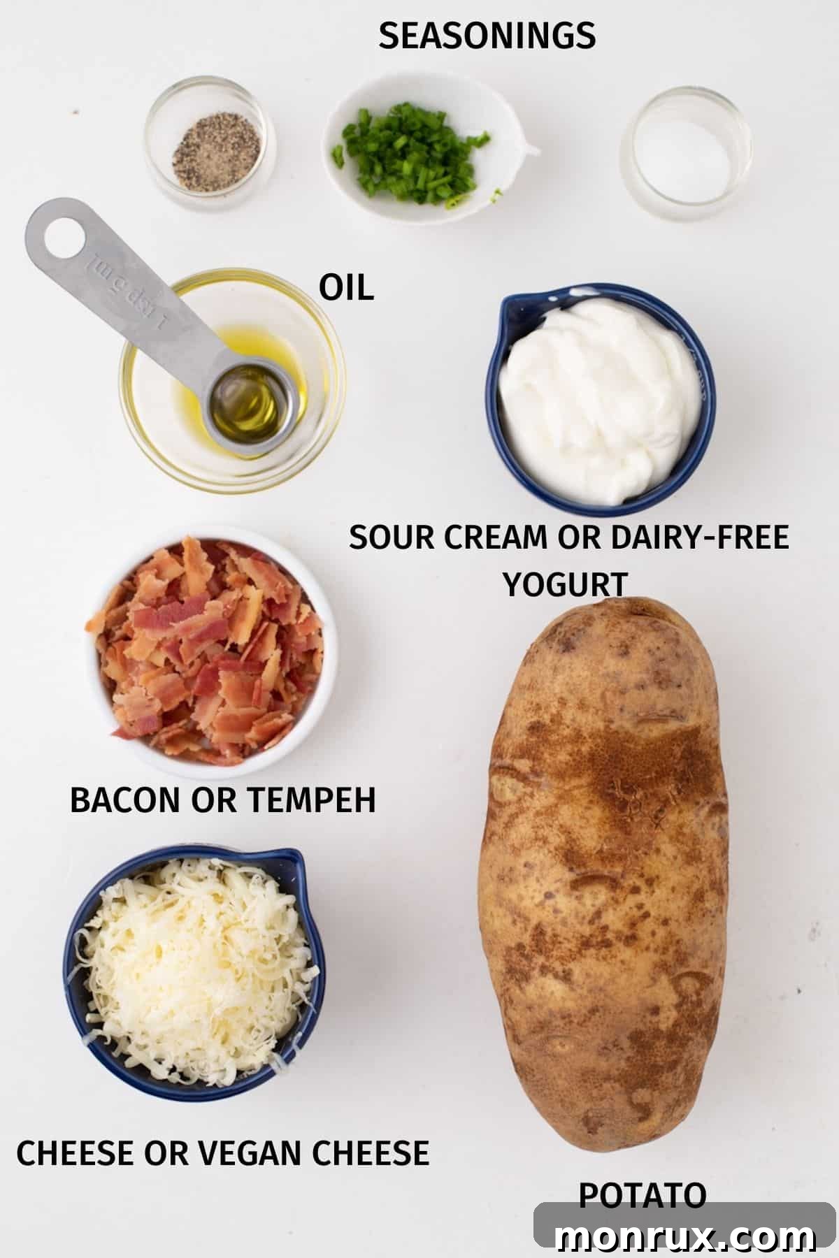 A selection of fresh ingredients neatly arranged on a rustic wooden board, including russet potatoes, a bottle of olive oil, a block of cheddar cheese, a tub of sour cream, and crispy bacon bits, all ready for the air fryer twice baked potato recipe.