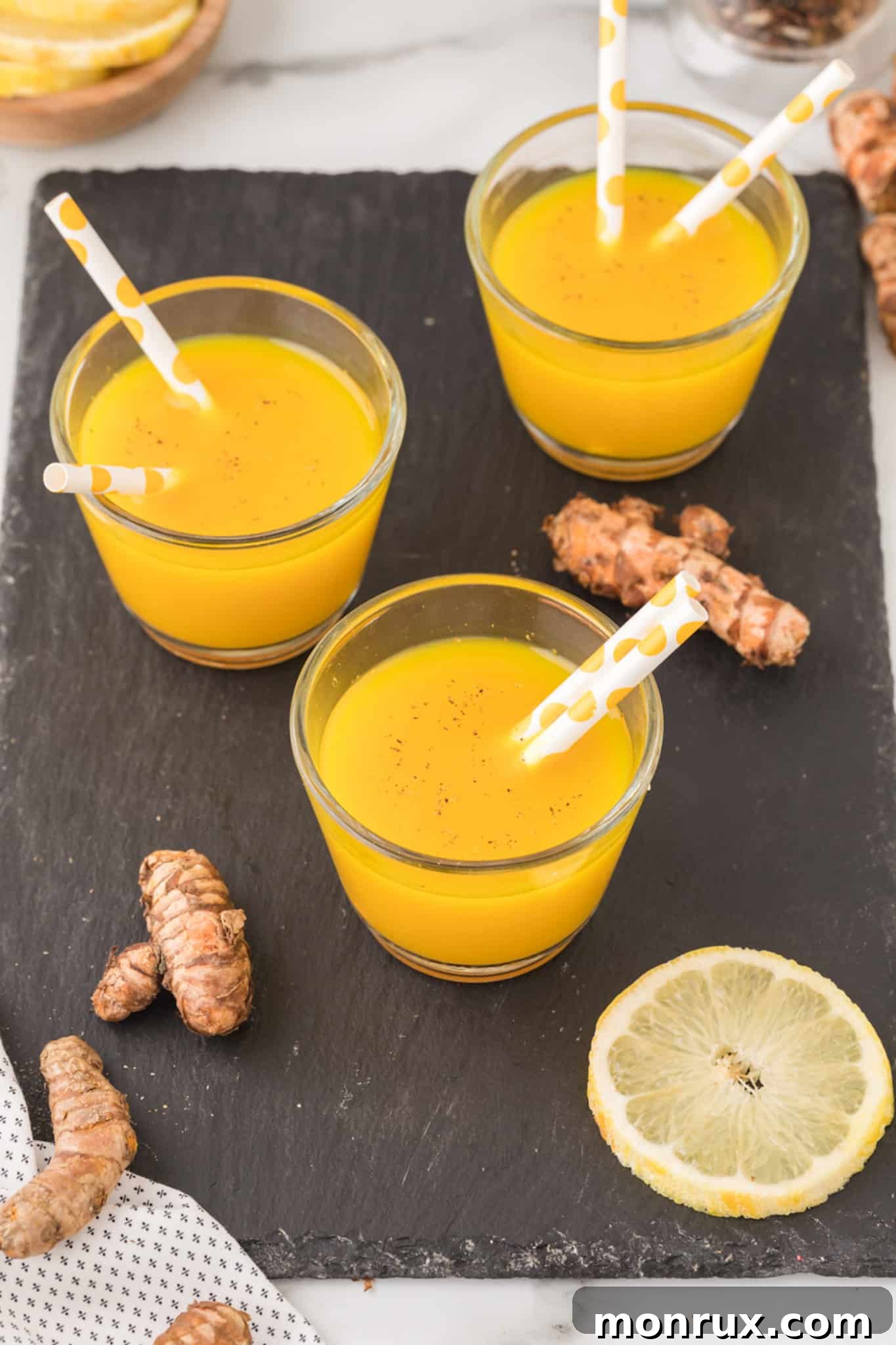 three glasses of yellow turmeric shot with straws on a table.
