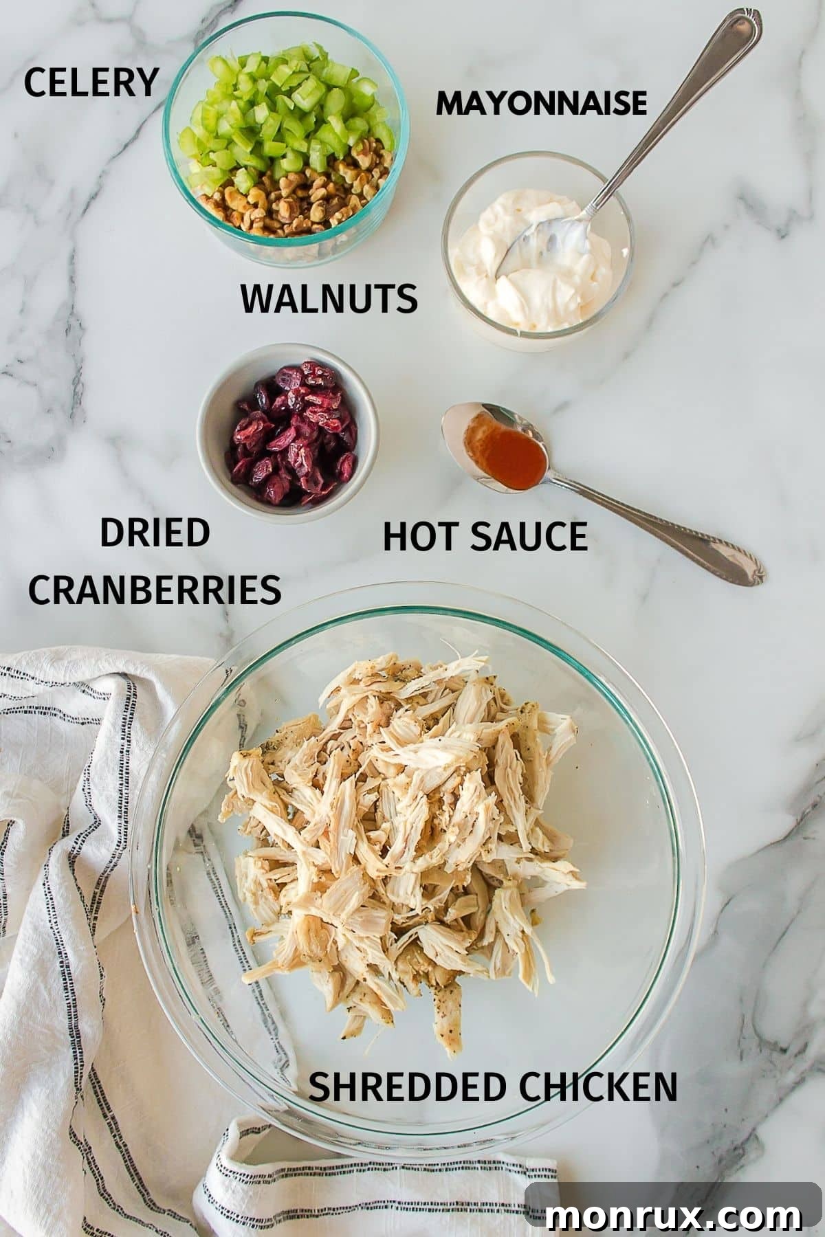 A flat lay photograph showcasing all the fresh and wholesome ingredients laid out for making cranberry walnut chicken salad, including chicken, walnuts, cranberries, celery, lemon, and mayonnaise.
