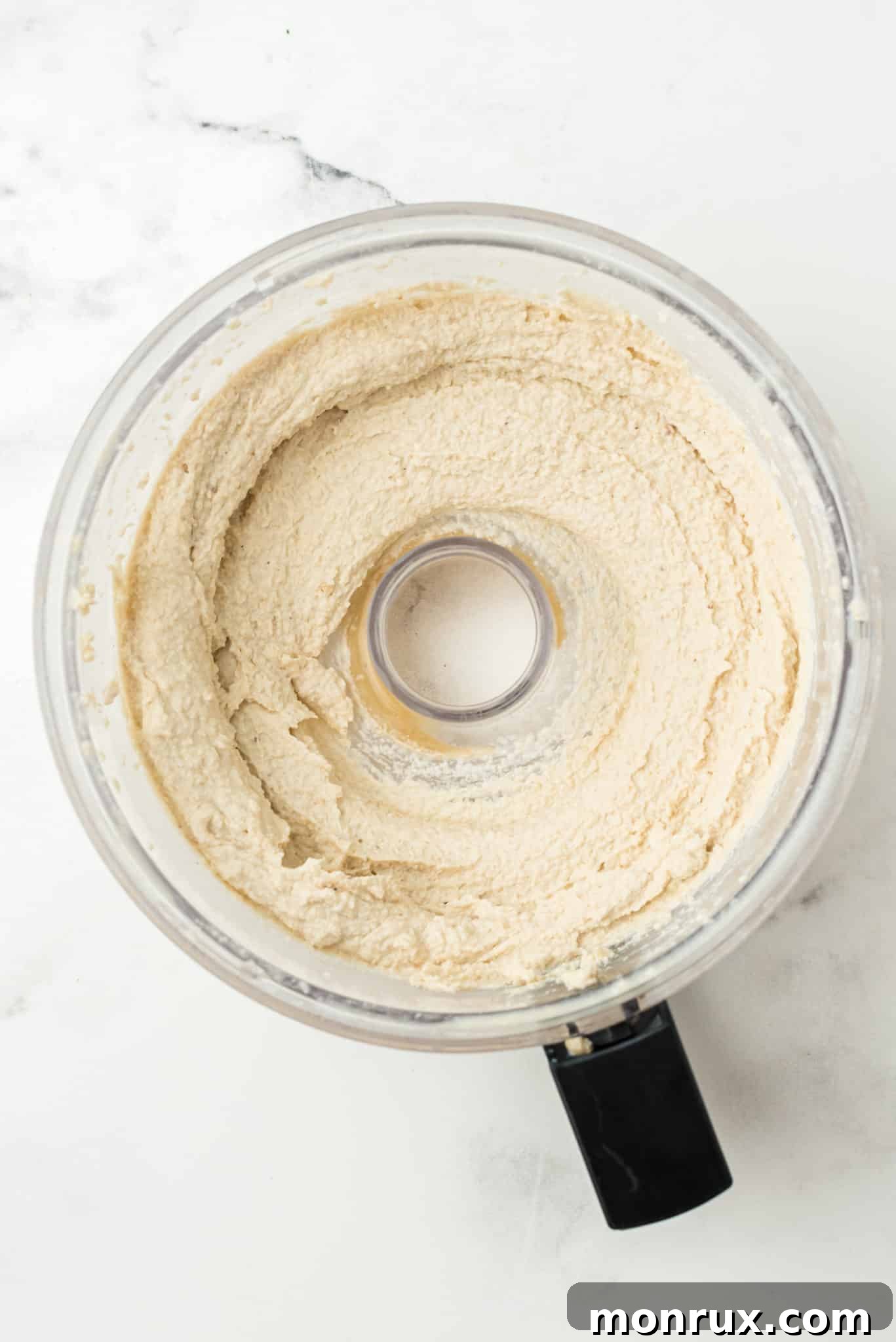 Creamy cashew hummus being blended smoothly inside a food processor bowl.