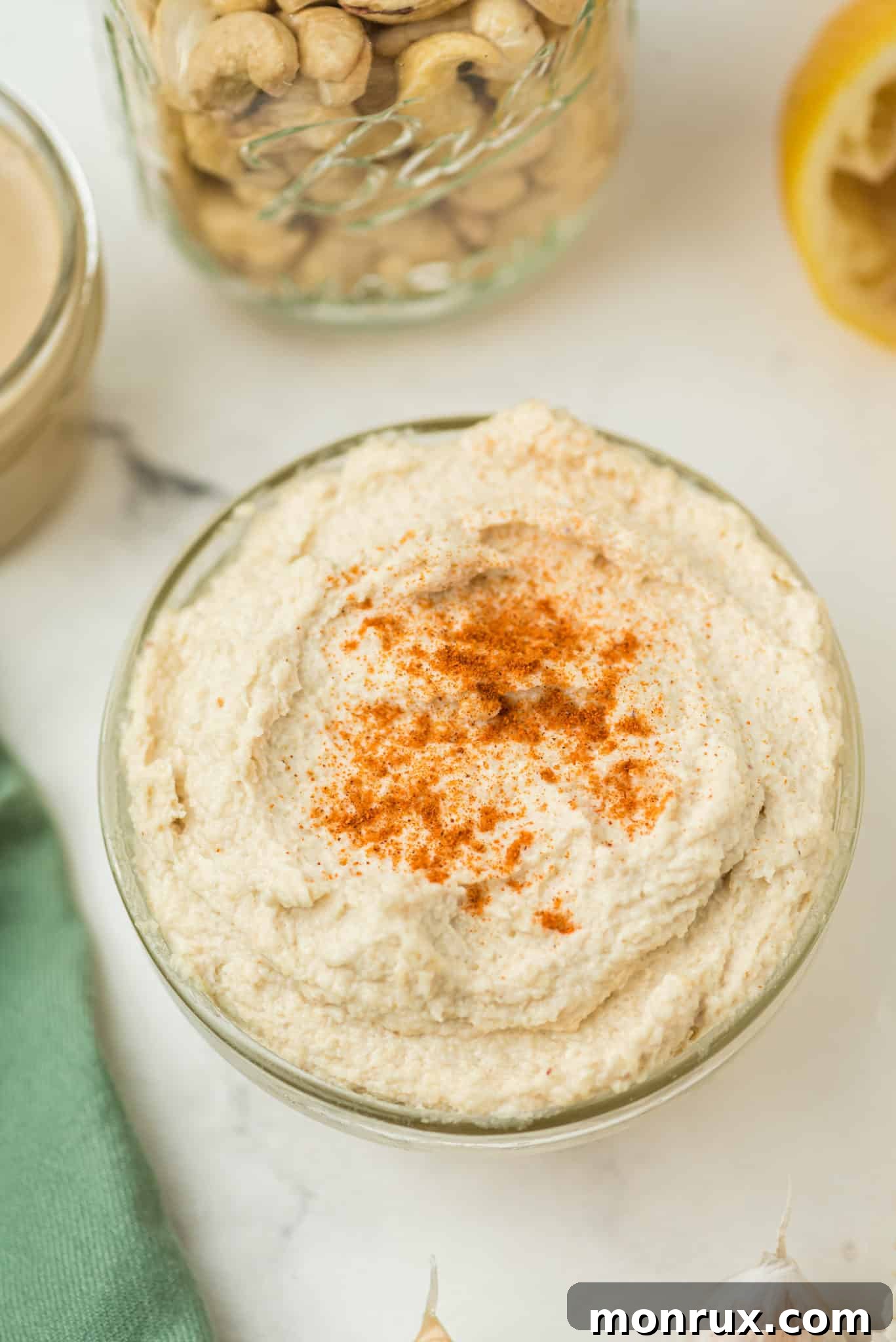 A serving bowl filled with creamy cashew hummus, topped generously with smoked paprika, against a rustic background.