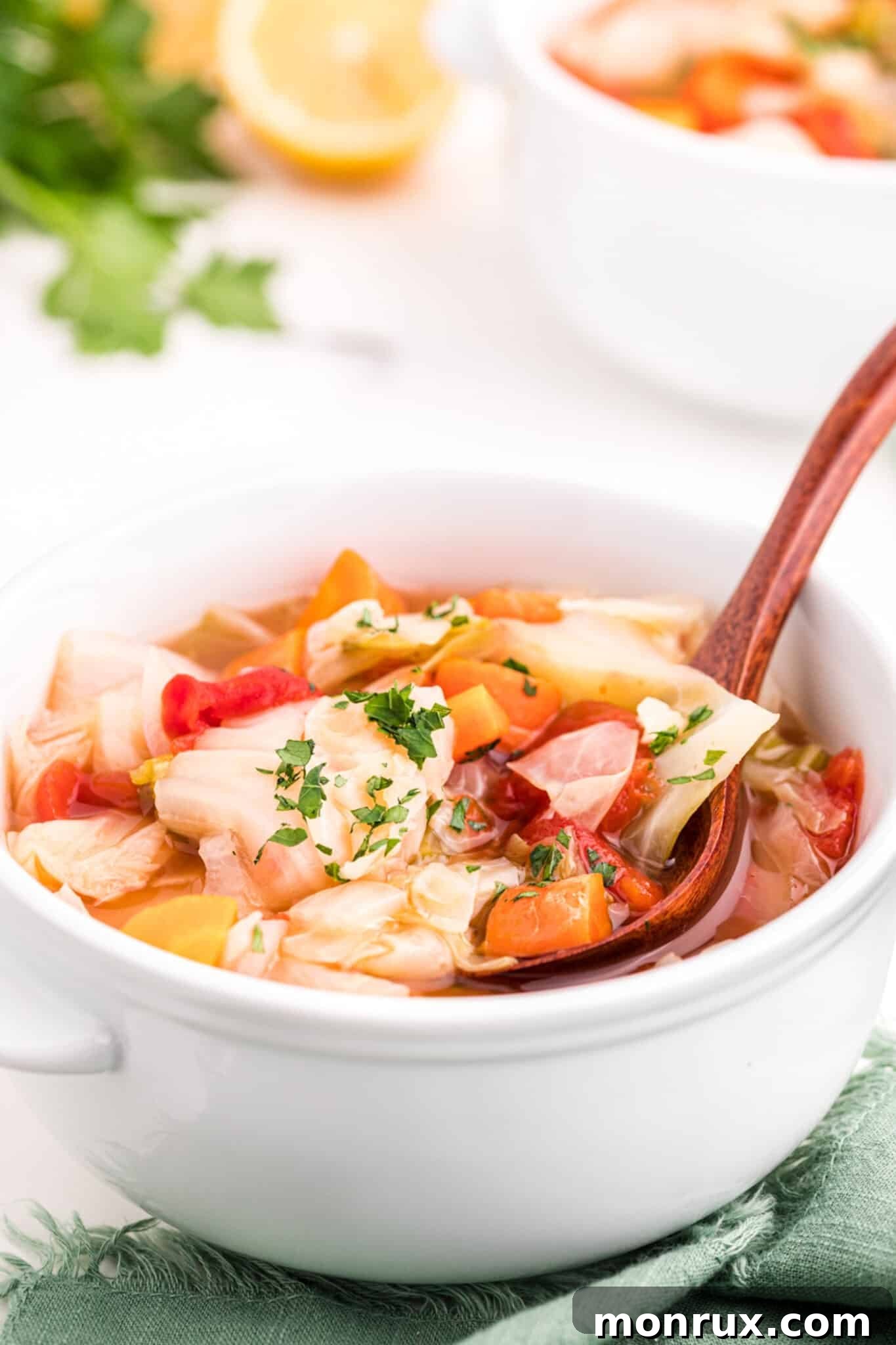 A bowl of finished cabbage soup, garnished with fresh parsley and served with a spoon.