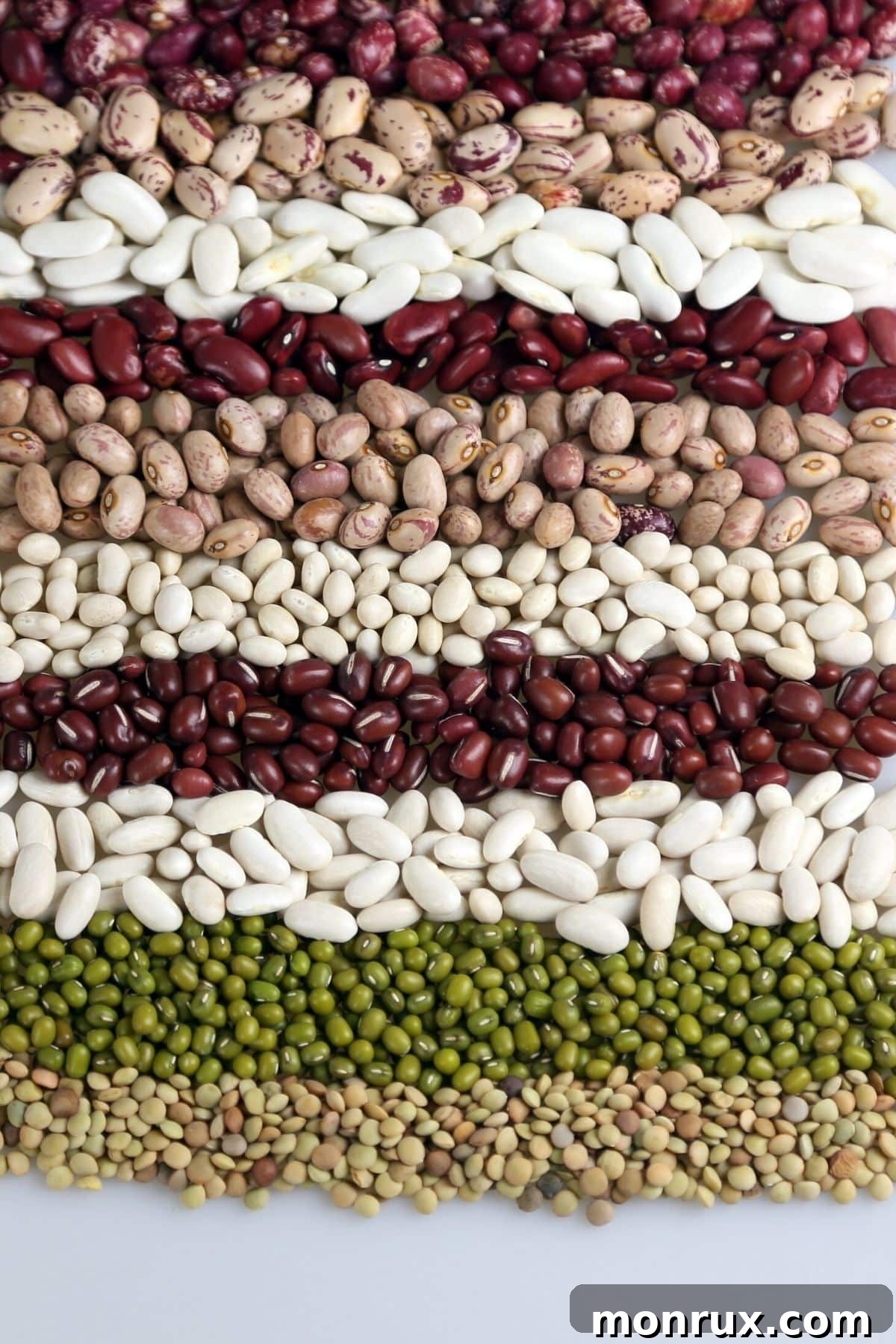 A diverse assortment of dried beans and peas, representing various legumes, on a textured surface.