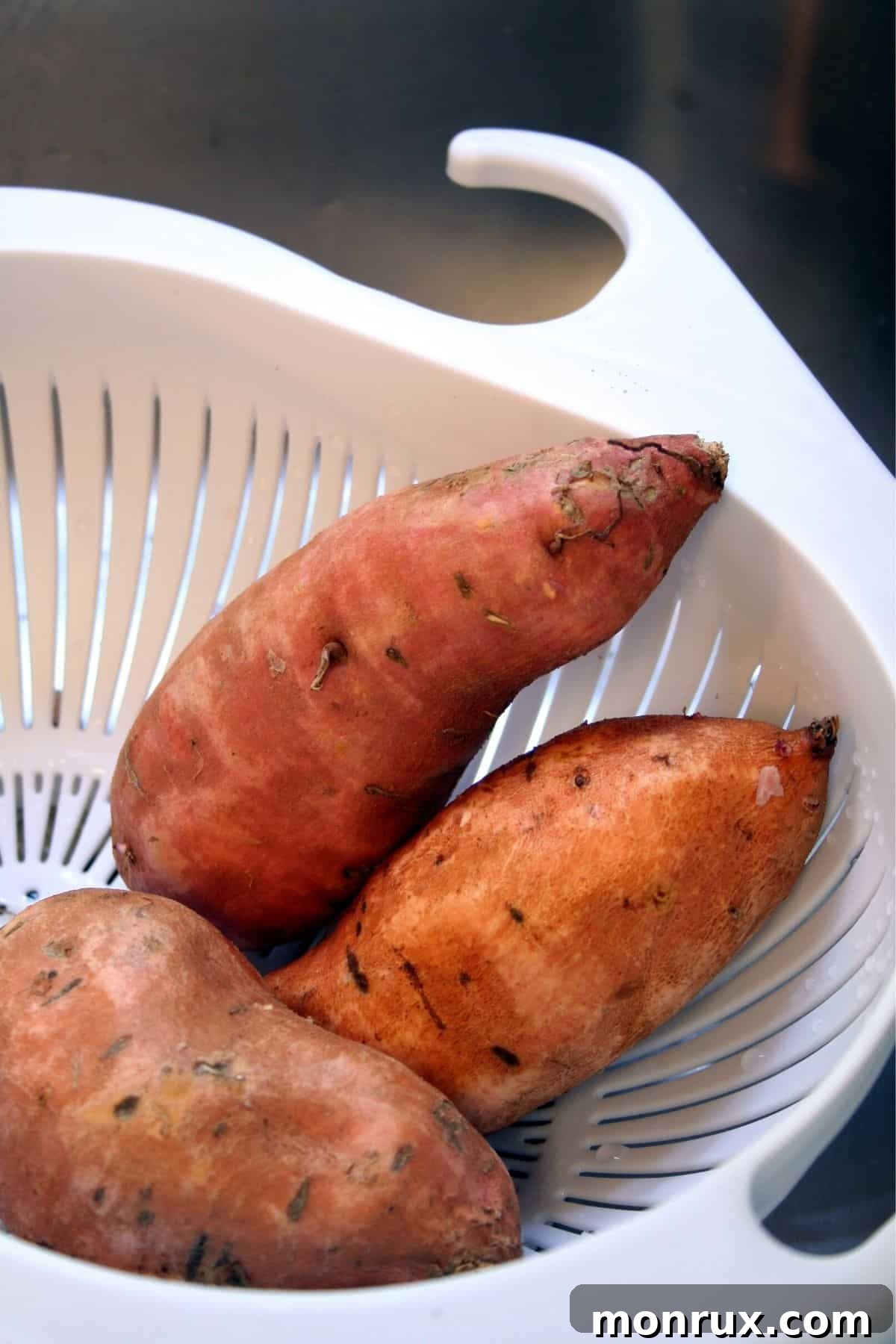 A colander brimming with fresh sweet potatoes, ready for preparation.
