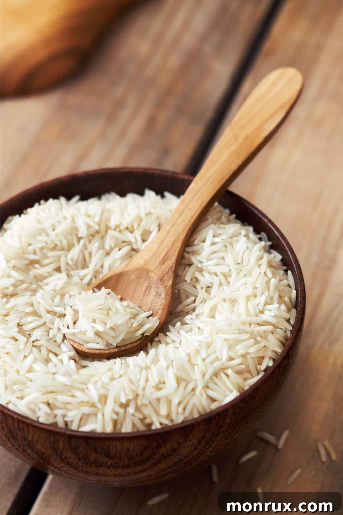 A wooden bowl filled with fluffy basmati rice, accompanied by a wooden spoon.
