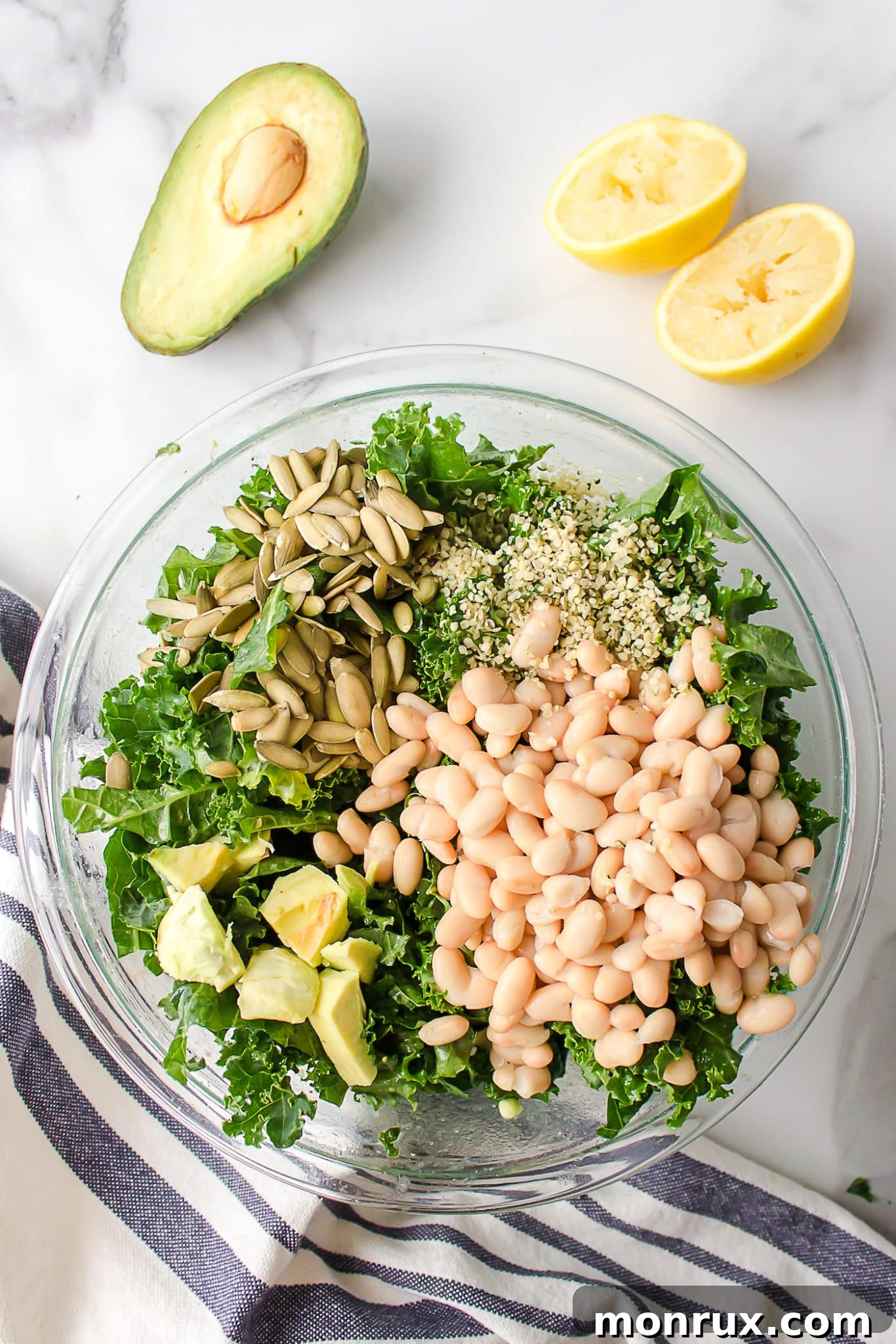 A close-up shot of chopped kale, white beans, avocado, and pumpkin seeds in a bowl, ready to be dressed and tossed.