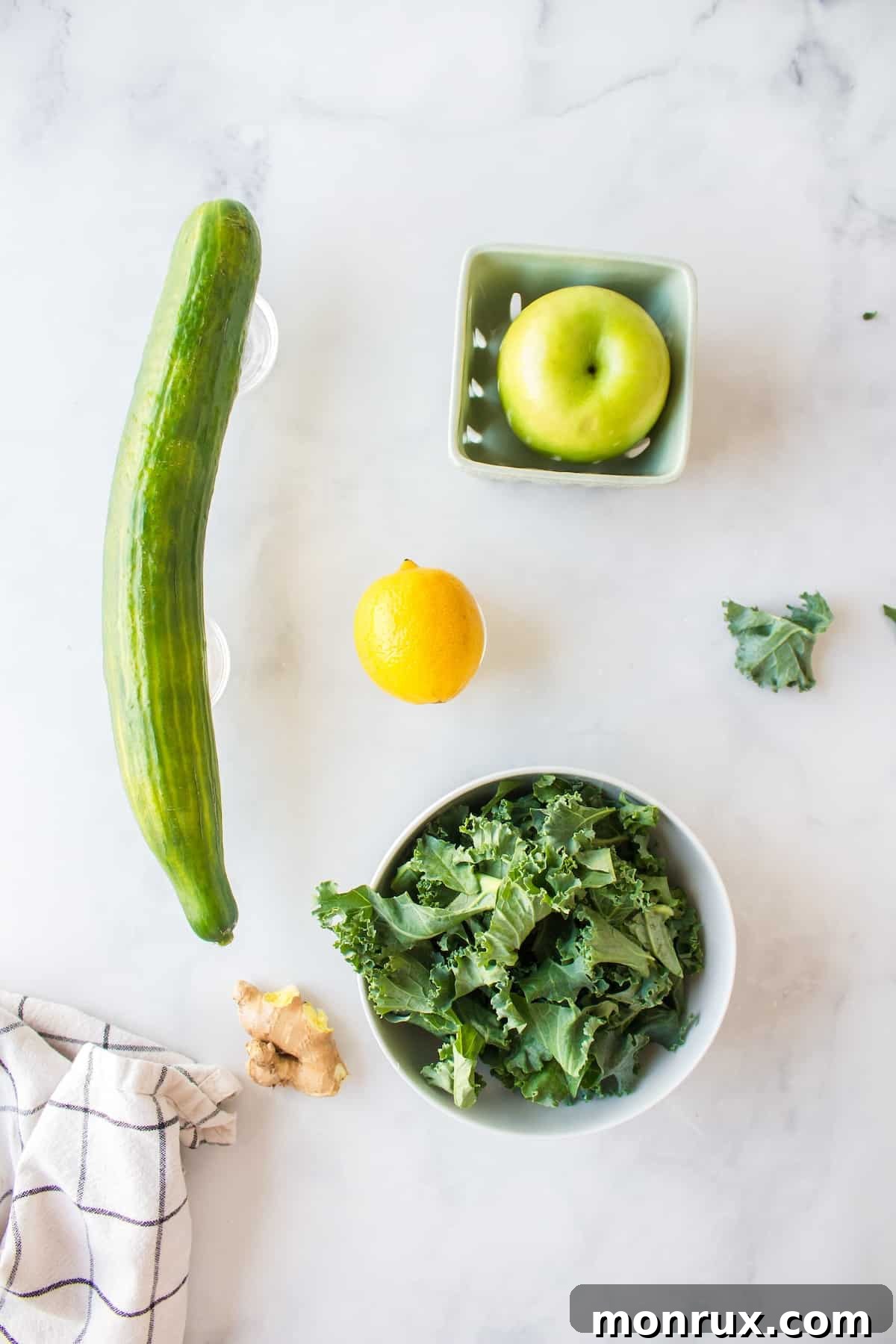 ingredients for making kale juice on table including kale, cucumber, apple, lemon, and ginger.