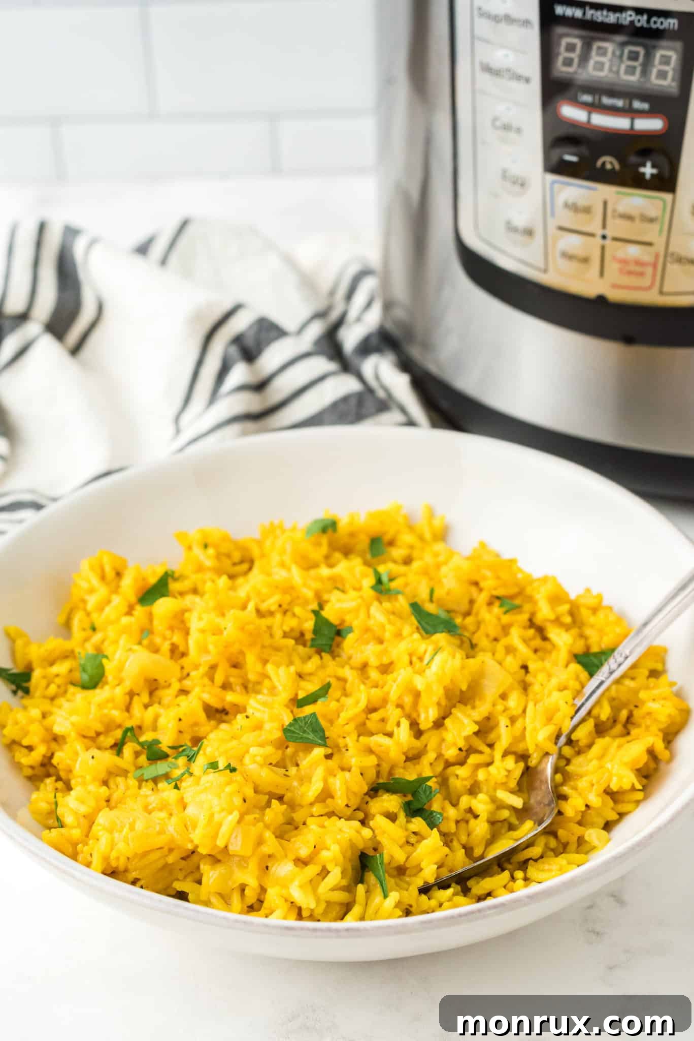 A beautifully presented bowl of Instant Pot yellow rice, garnished with fresh herbs, and a serving spoon ready to portion. The vibrant yellow color of the rice is prominent.