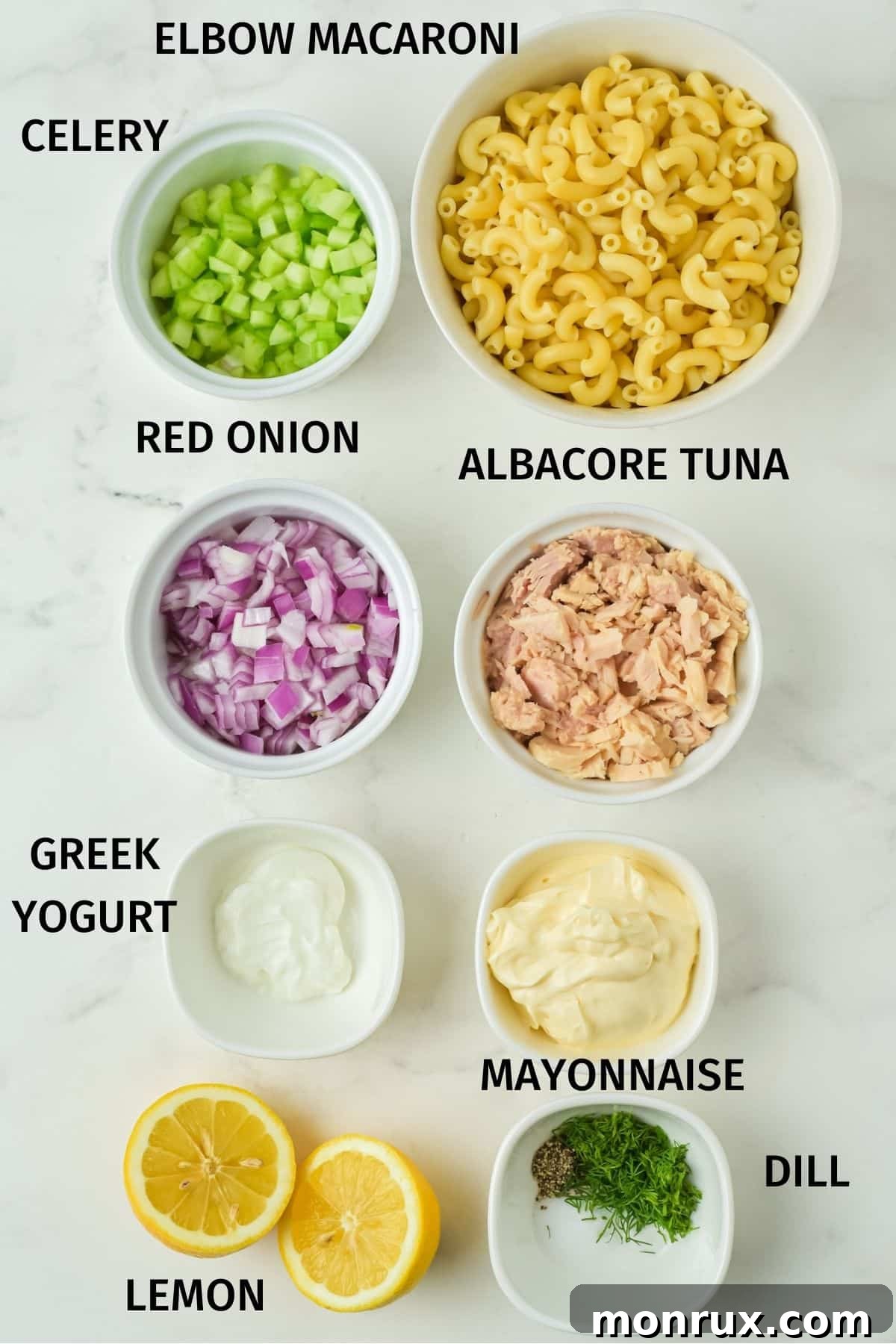 A flat lay image displaying all the fresh ingredients for tuna pasta salad: elbow macaroni, diced celery, red onion, canned tuna, Greek yogurt, mayonnaise, fresh lemon, and dill.