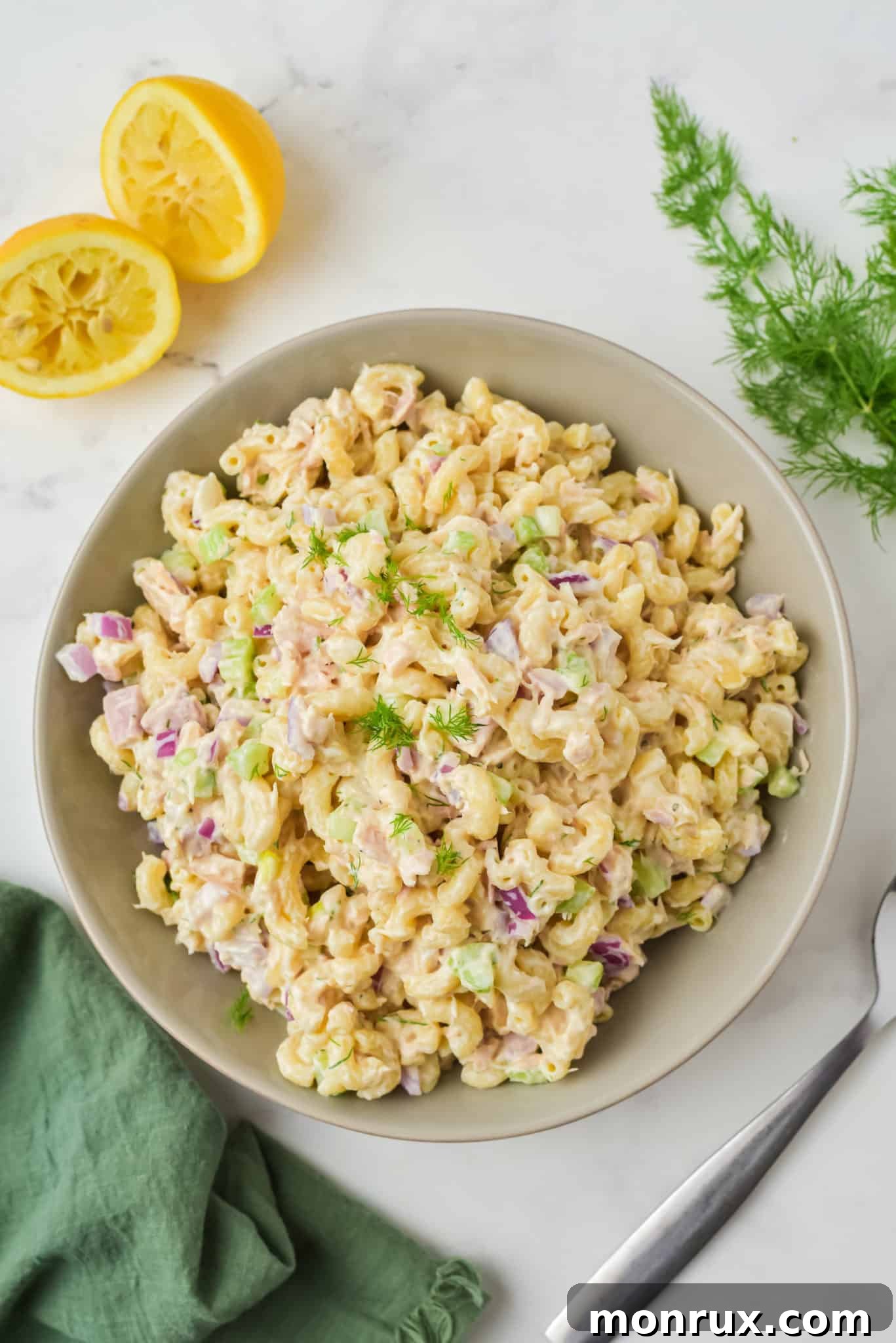 A large, inviting bowl of gluten-free and healthy tuna pasta salad, garnished with fresh green herbs.