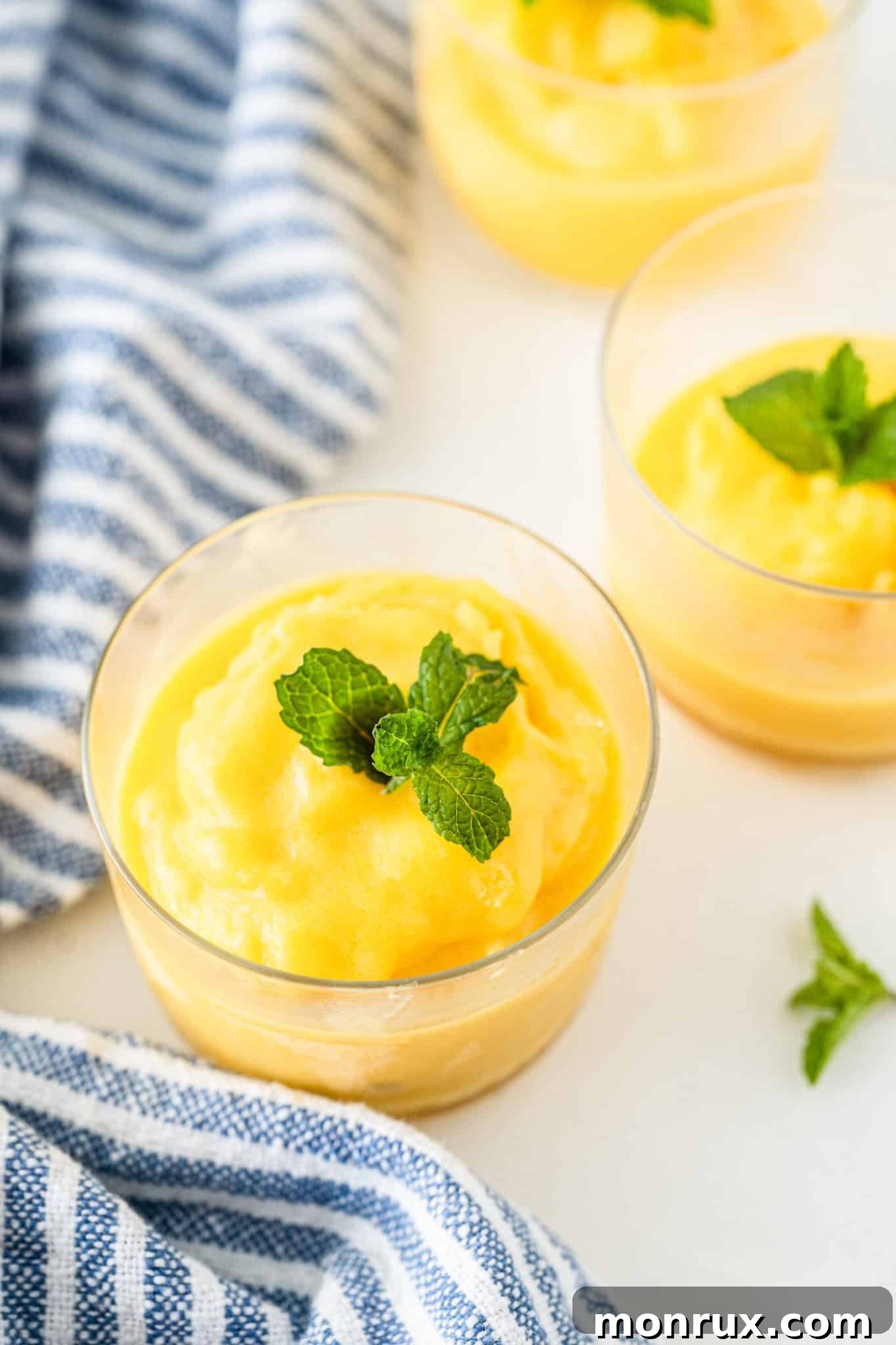 A elegant glass dish filled with vibrant orange mango sorbet, garnished with a mint leaf.