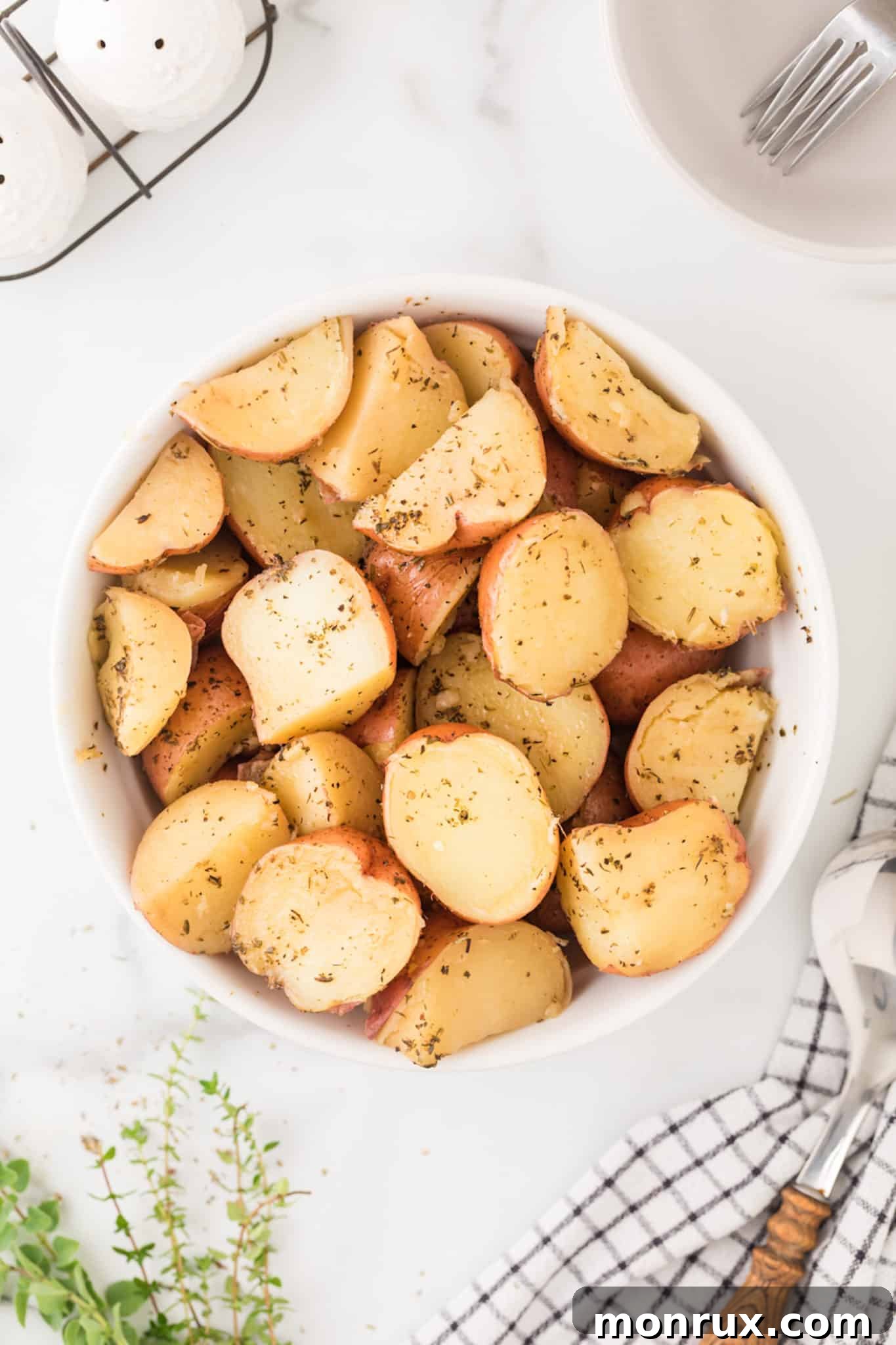 A rustic bowl filled with golden roasted red potatoes, garnished with fresh herbs.