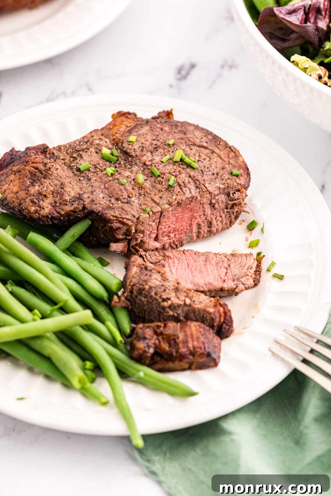 Air fried filet mignon served on a plate with vibrant green beans, showcasing a perfectly cooked interior.
