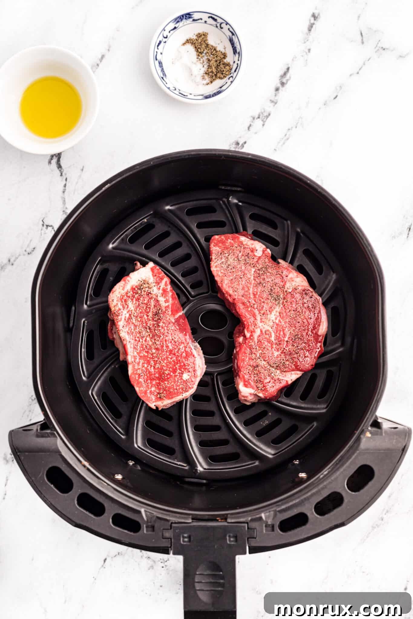 Seasoned uncooked filet mignon steaks placed neatly inside an air fryer basket, ready for cooking.