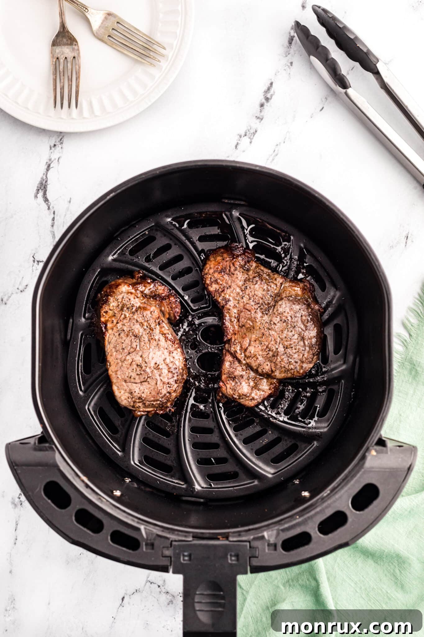 Two perfectly cooked air fryer filet mignon steaks inside the air fryer basket after cooking.