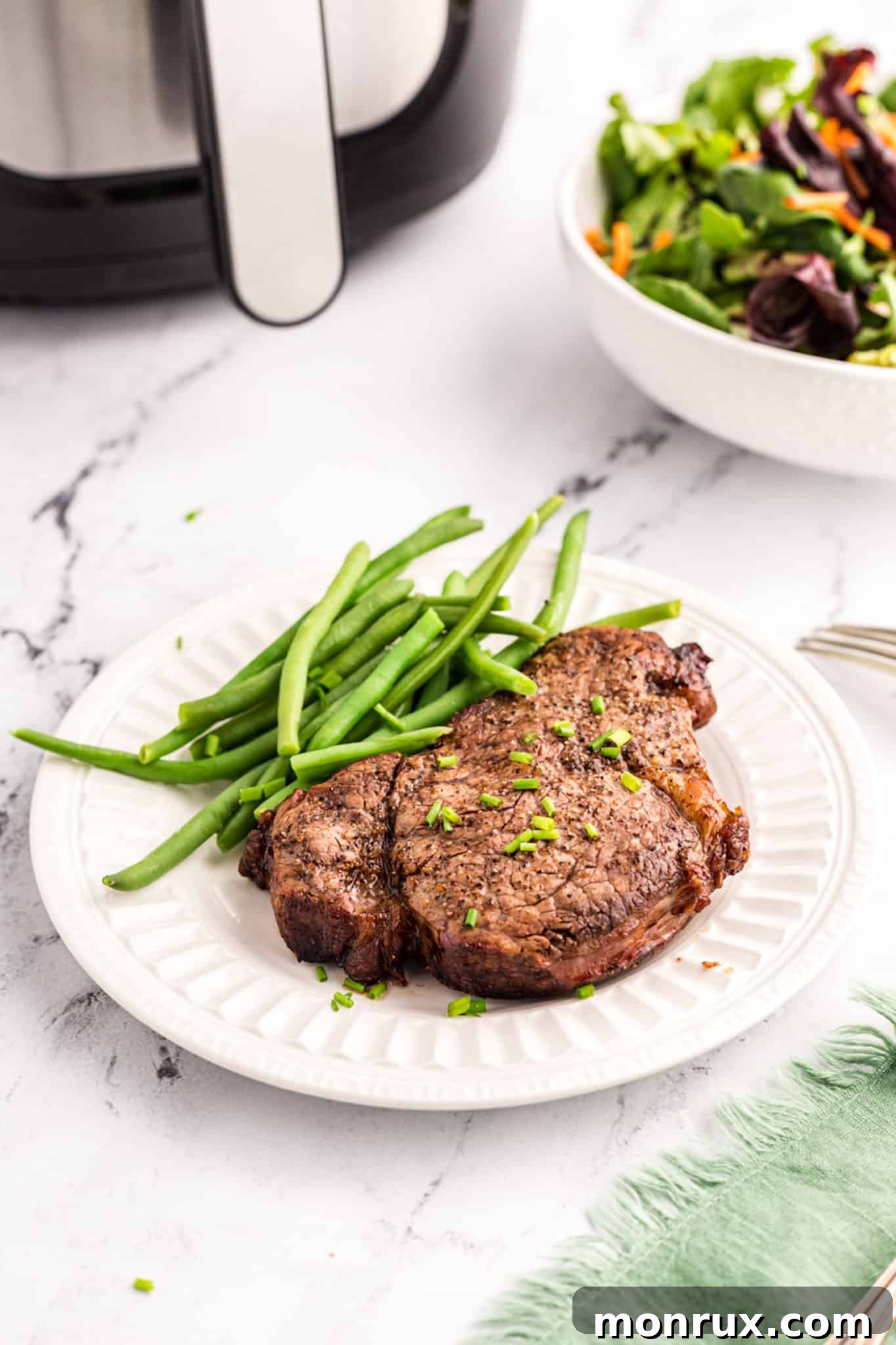 A beautifully cooked air fryer filet mignon, sliced to reveal a perfect medium-rare, served with crisp green beans on a white plate.