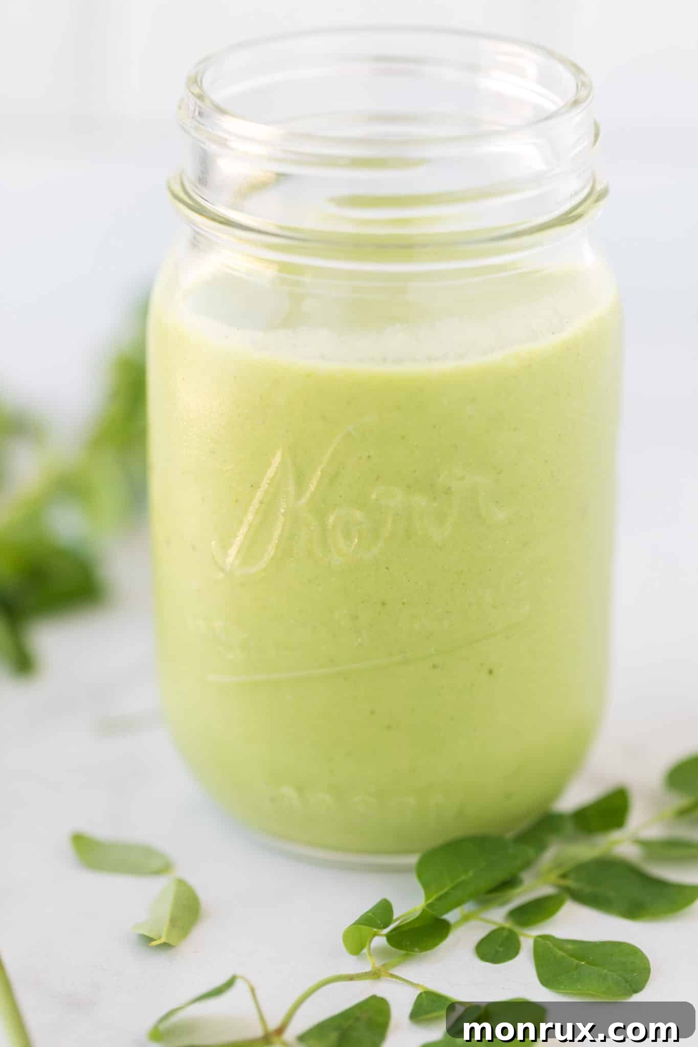 Moringa smoothie in a large glass jar, garnished with a few fresh moringa leaves.