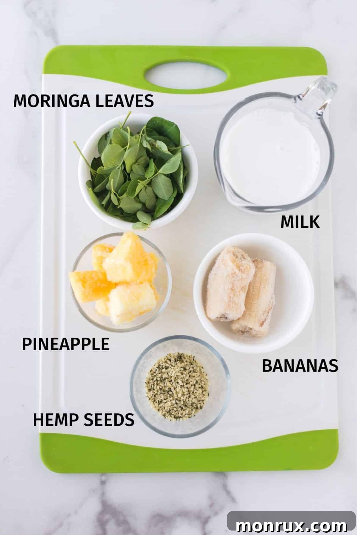 Moringa smoothie ingredients in small bowls on the kitchen counter, including fresh moringa, bananas, pineapple, hemp seeds, and almond milk.