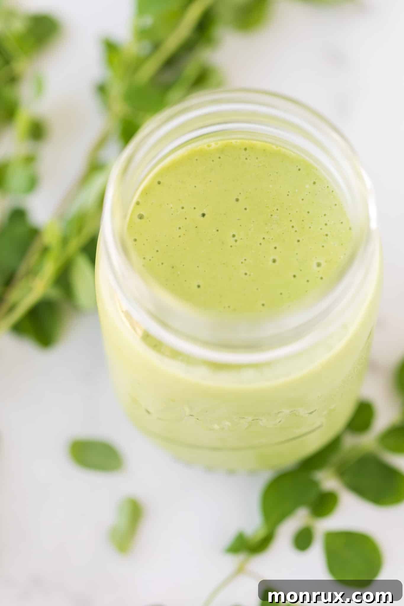 Finished moringa smoothie in a glass jar with a straw, ready to drink.