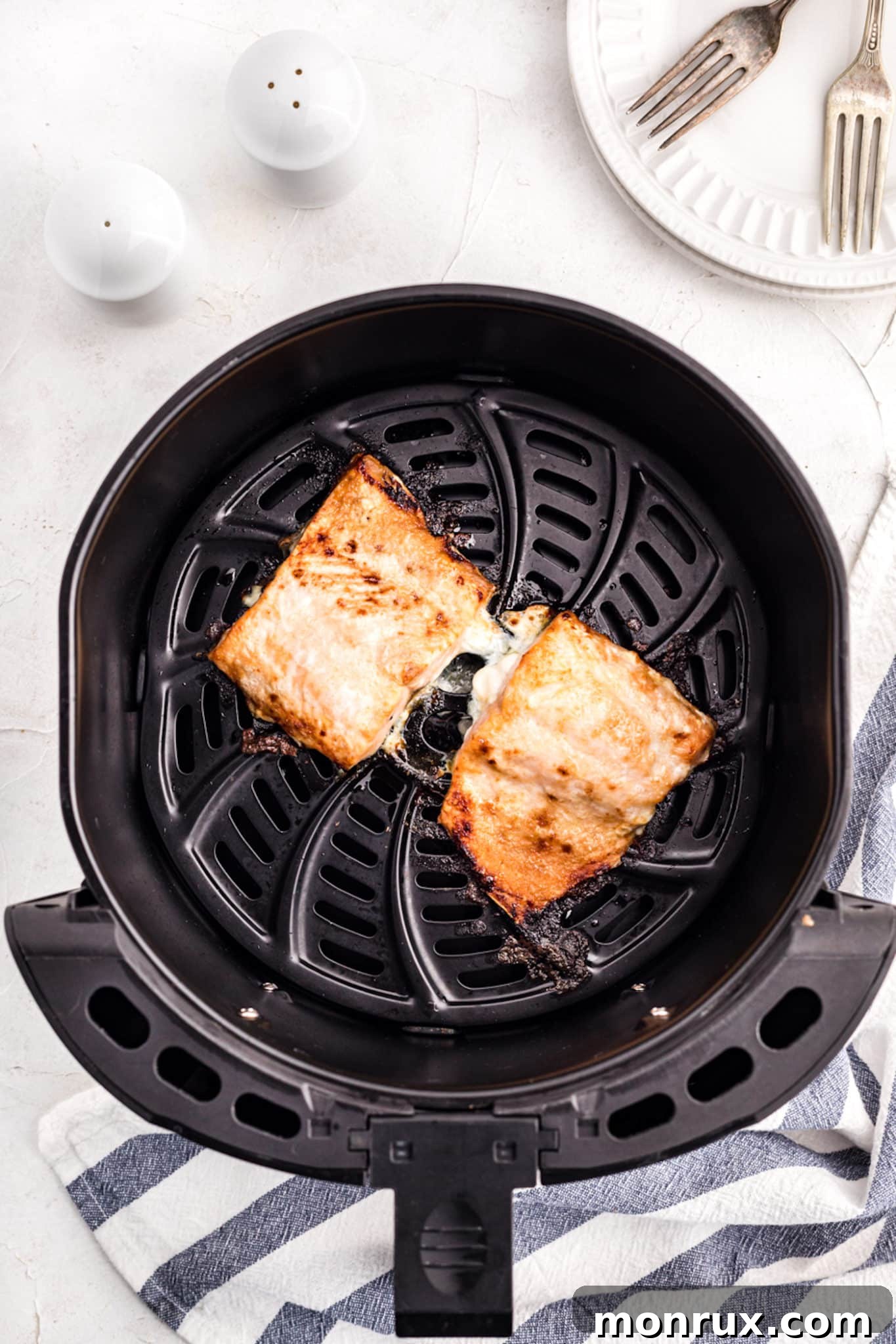cooked frozen salmon fillets inside air fryer basket, showing crispy edges.