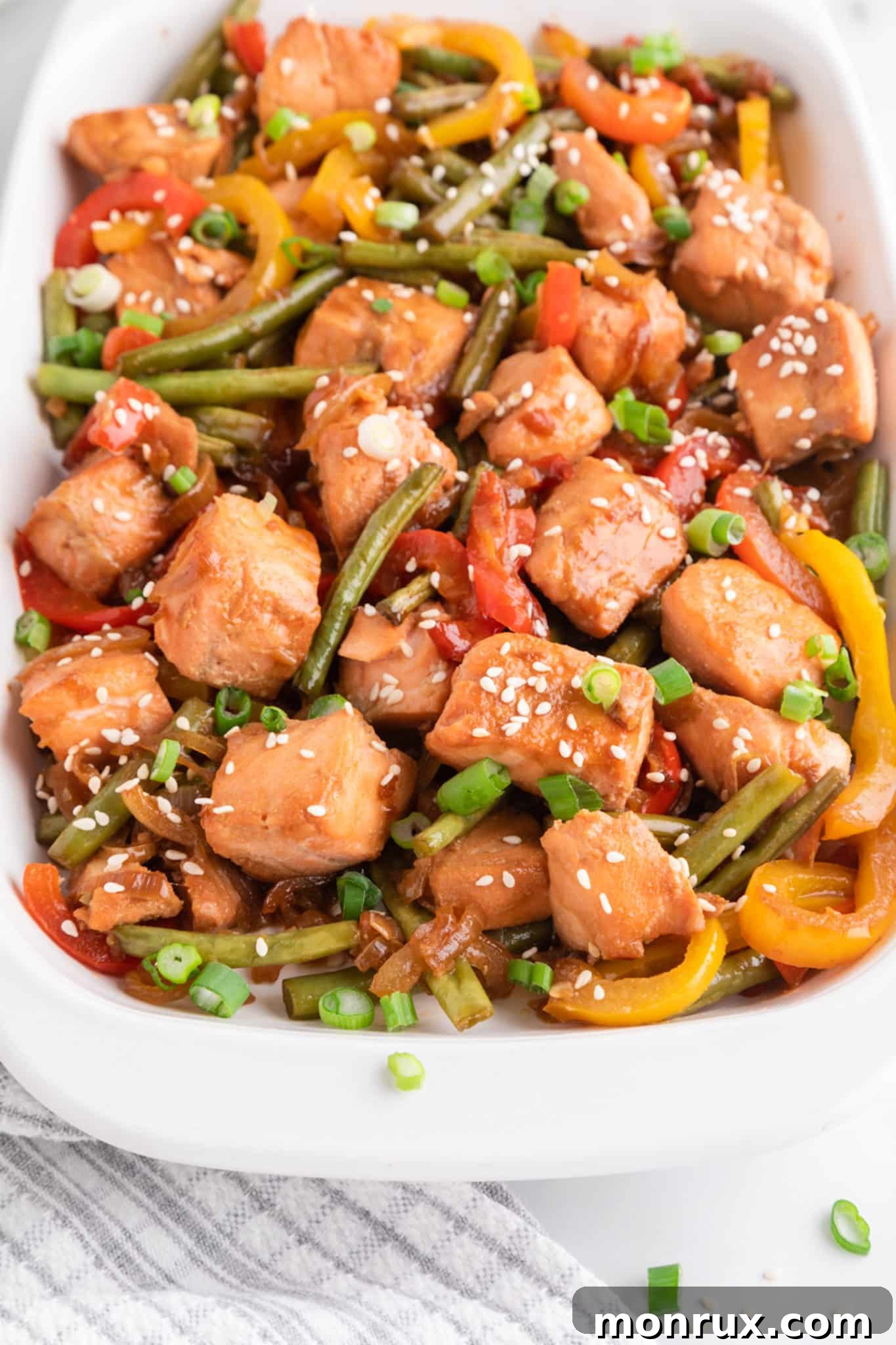 Close up of a vibrant salmon and vegetable stir-fry, presented in an elegant white serving dish, highlighting the fresh ingredients and rich colors.