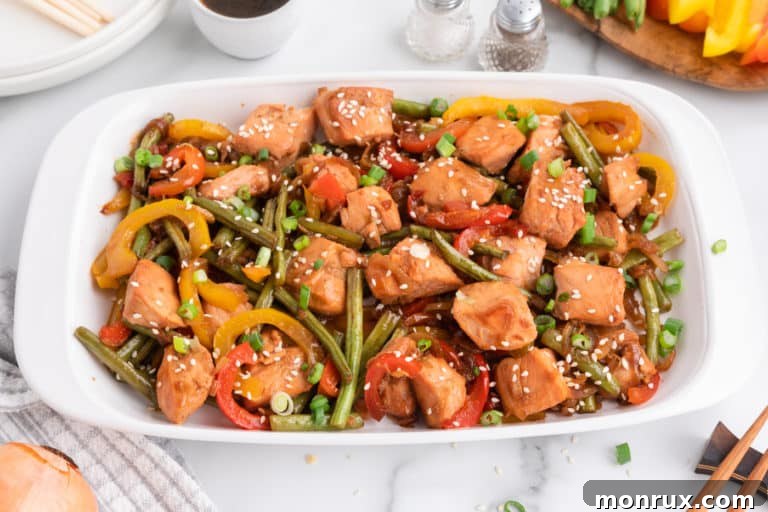 A rectangular serving dish filled with a generous portion of colorful salmon stir-fry, garnished with fresh herbs.