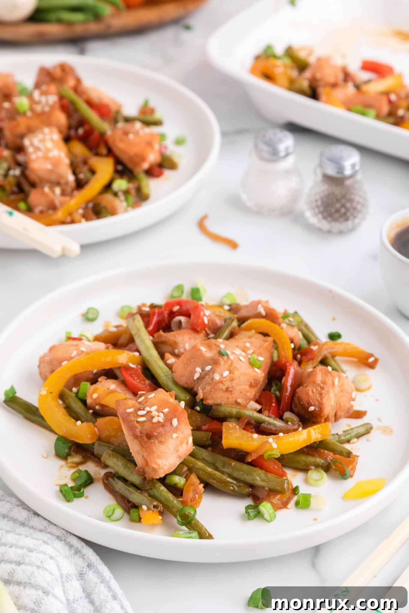 Two pristine white plates, each artfully arranged with a generous serving of salmon and vegetable stir-fry, ready to be enjoyed on a clean white table.