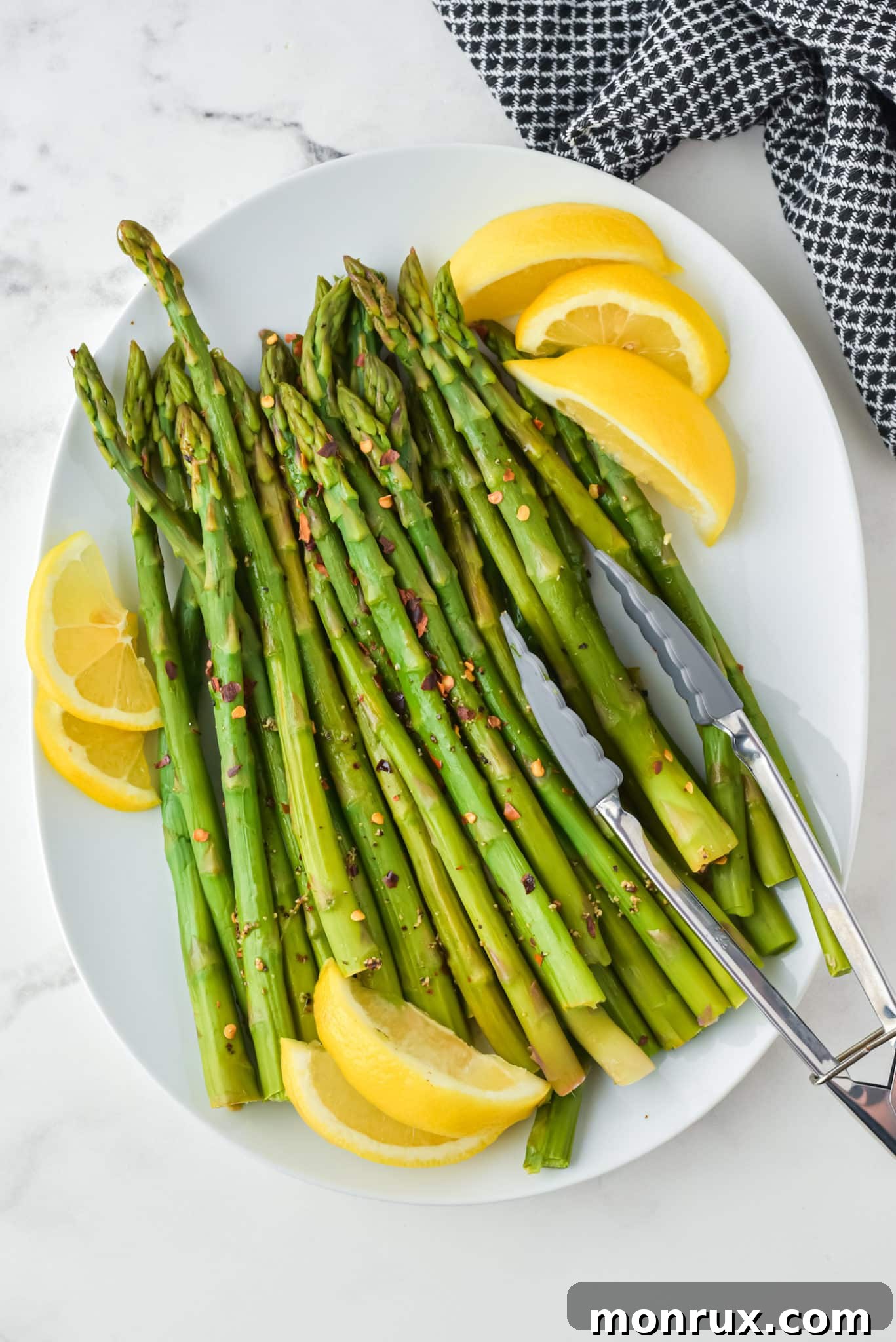 An oval white platter with perfectly cooked Instant Pot asparagus, garnished with fresh lemon wedges, and serving tongs.