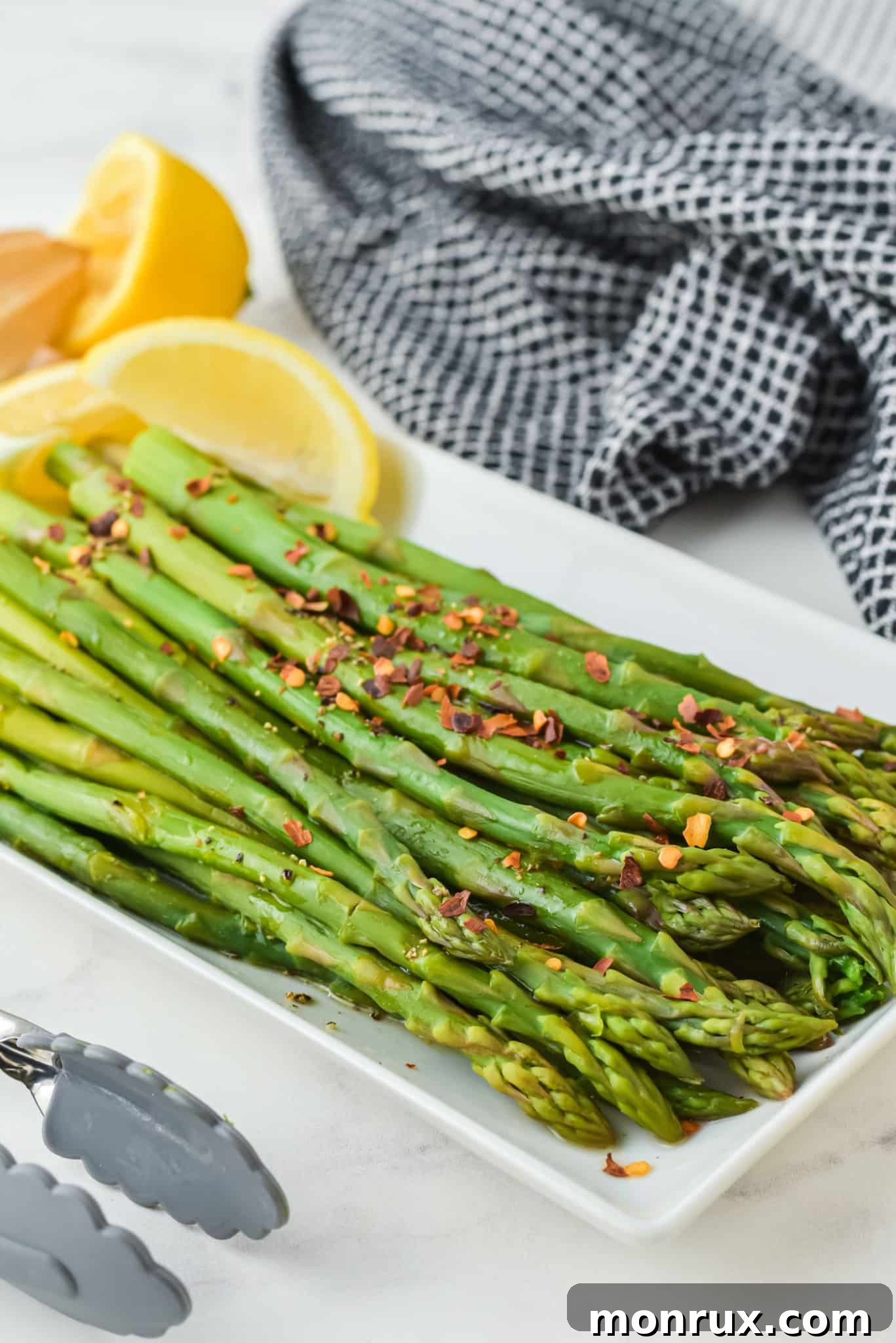 Red chili flakes generously sprinkled on a bed of vibrant green asparagus spears arranged on a white serving platter.