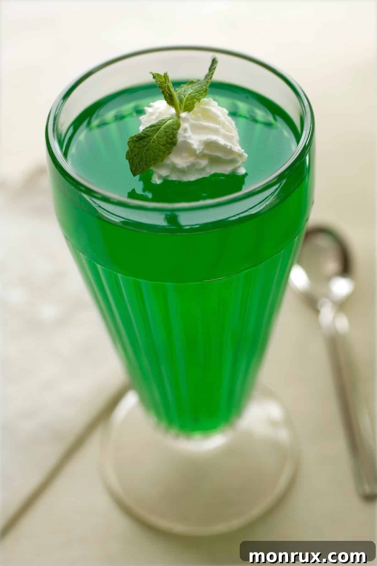 A cup of vibrant green Jello topped with a swirl of whipped cream, a comforting soft food option.