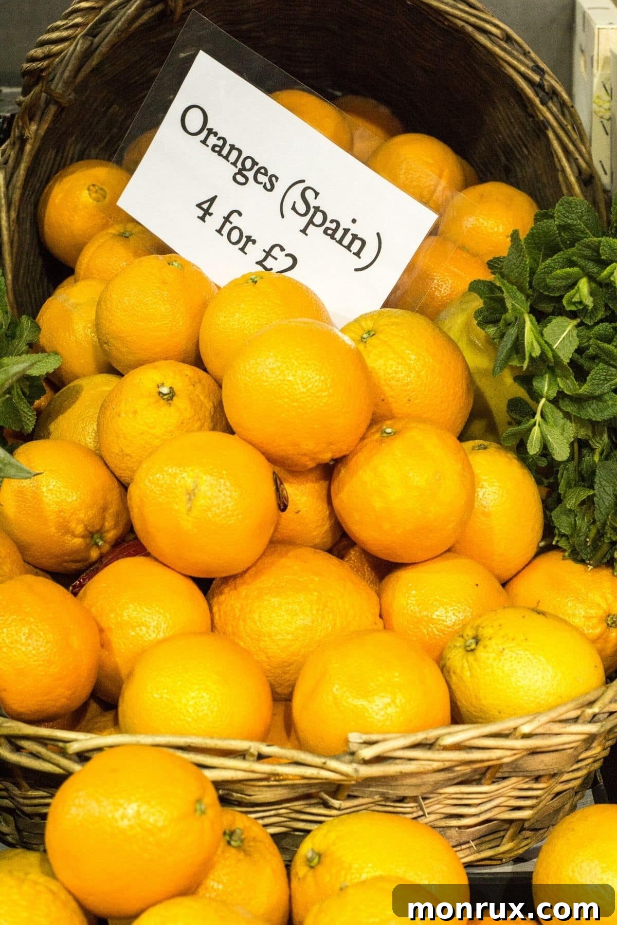 A rustic basket overflowing with freshly harvested Spanish oranges, complete with a market price tag, ready for sale.