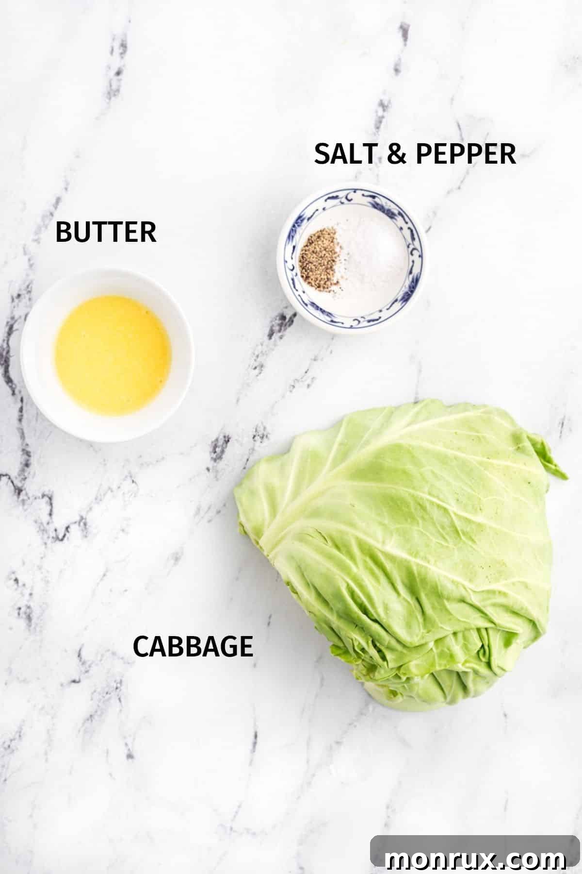 A flat lay photograph showcasing all the simple ingredients required for air fryer cabbage, including a fresh head of cabbage, butter, salt, and pepper.