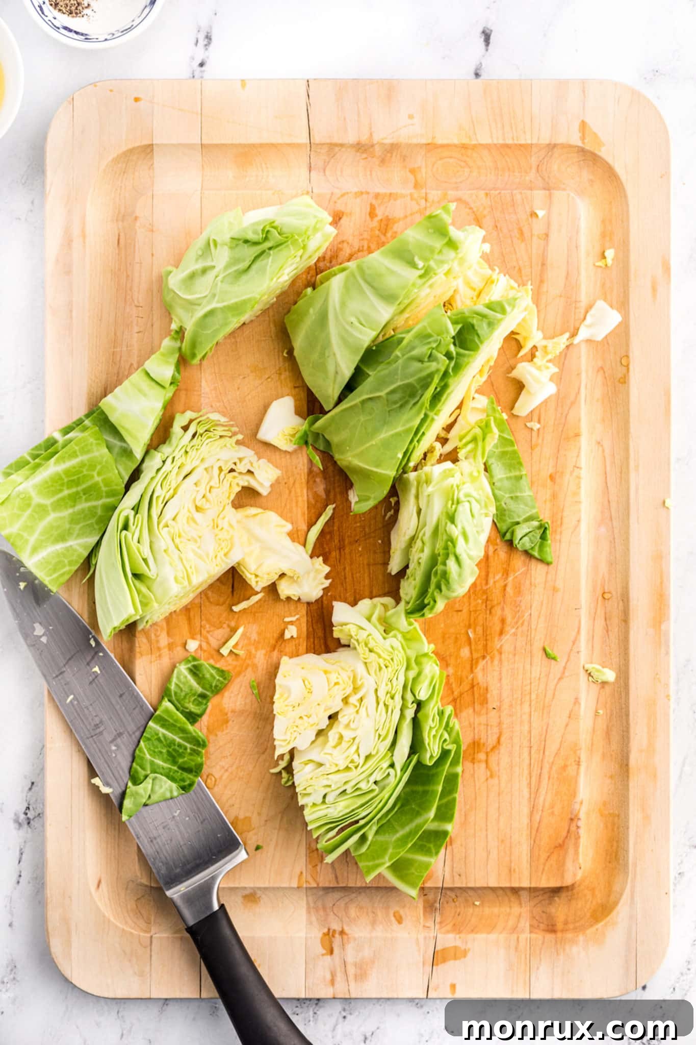 A chef's knife rests beside a perfectly cut head of cabbage on a rustic wood cutting board, showcasing the ideal chopping size for air frying.