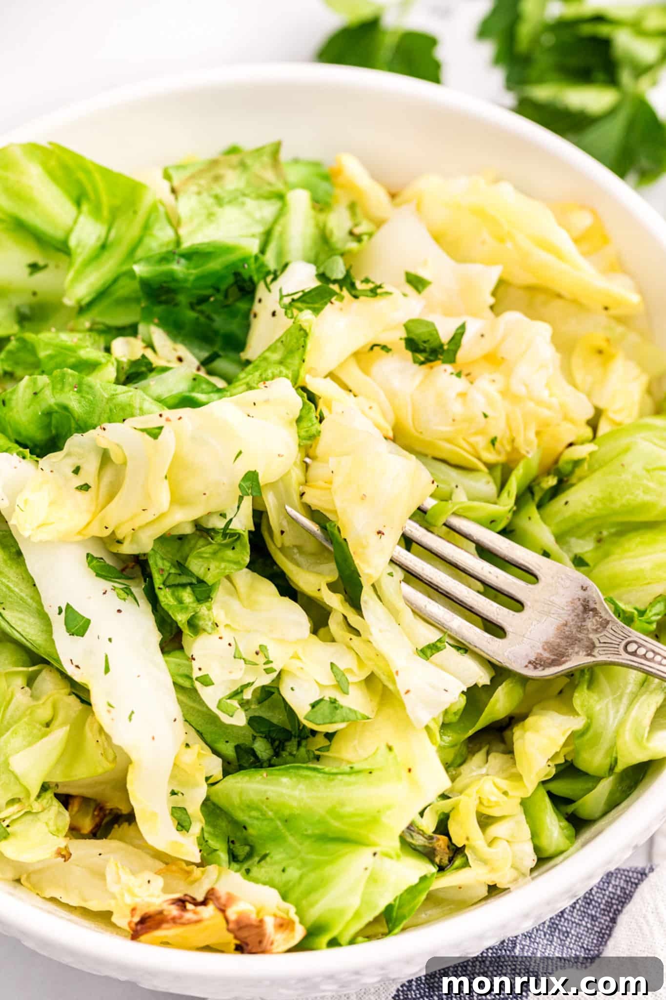 A fork piercing tender, golden-brown air fryer cabbage in a clean white ceramic bowl, highlighting its crispy texture.