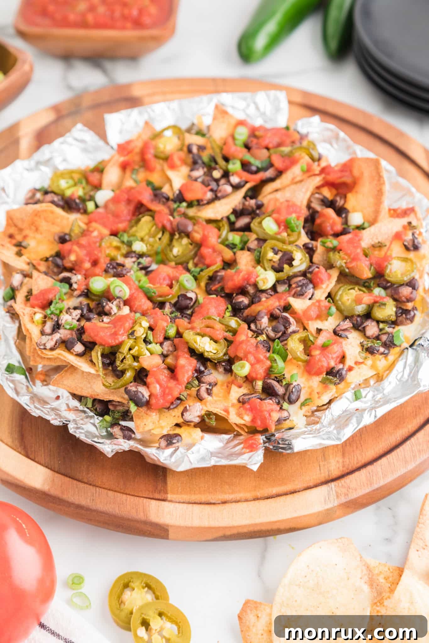 Air fryer nachos on homemade tortilla chips on a round wooden board, garnished with fresh cilantro and lime wedges.
