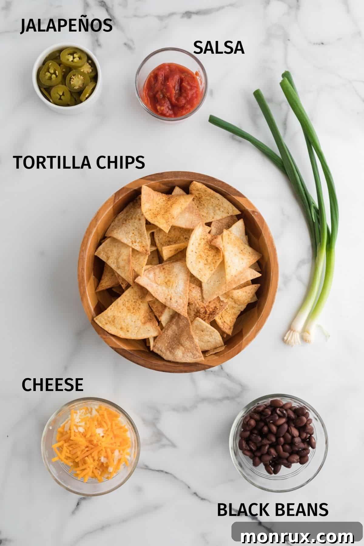 Tortilla chips and various toppings for nachos in small bowls on a white surface, ready for assembly.