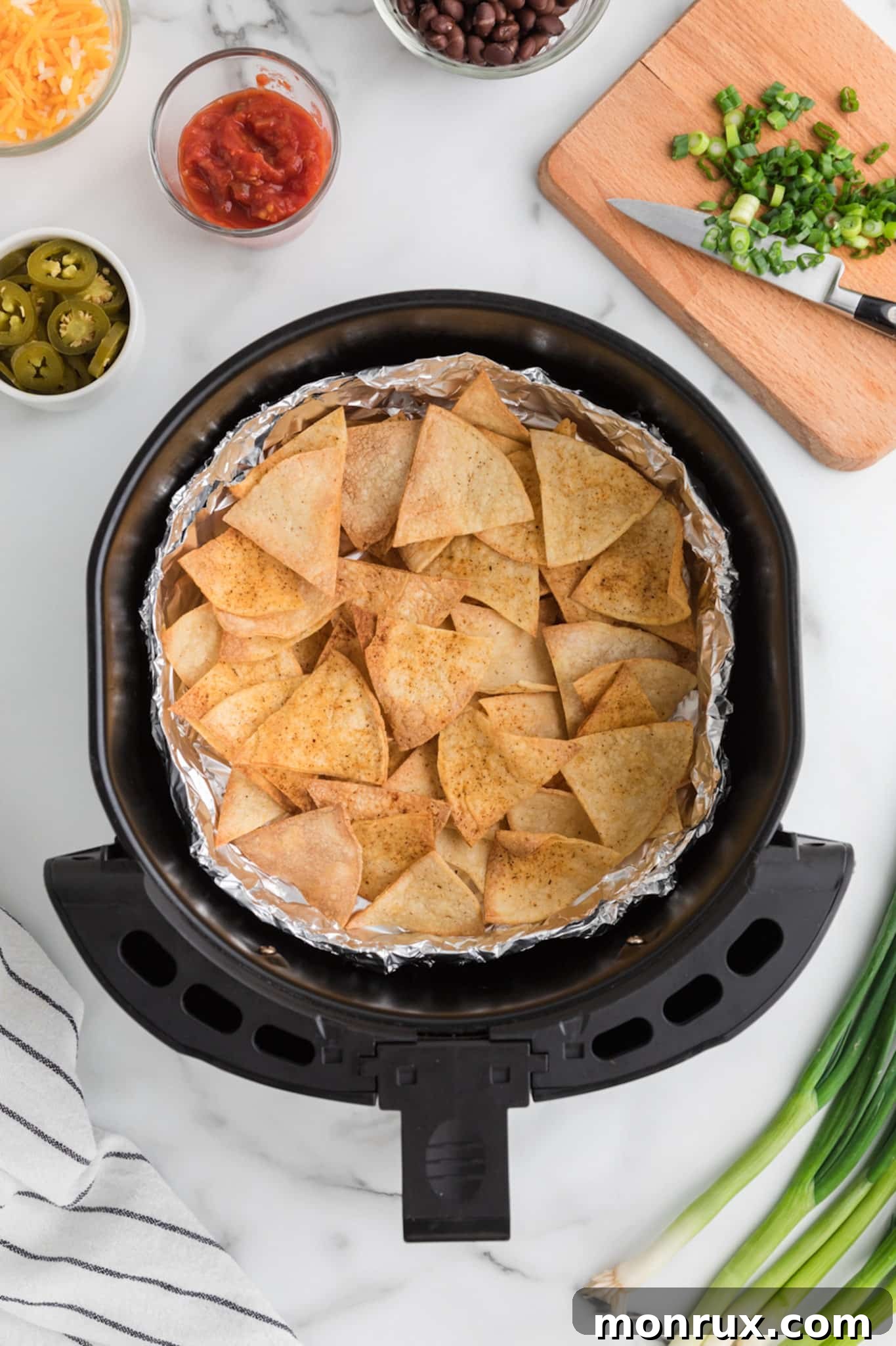 Top view of an air fryer basket lined with foil and filled with a single layer of homemade tortilla chips.