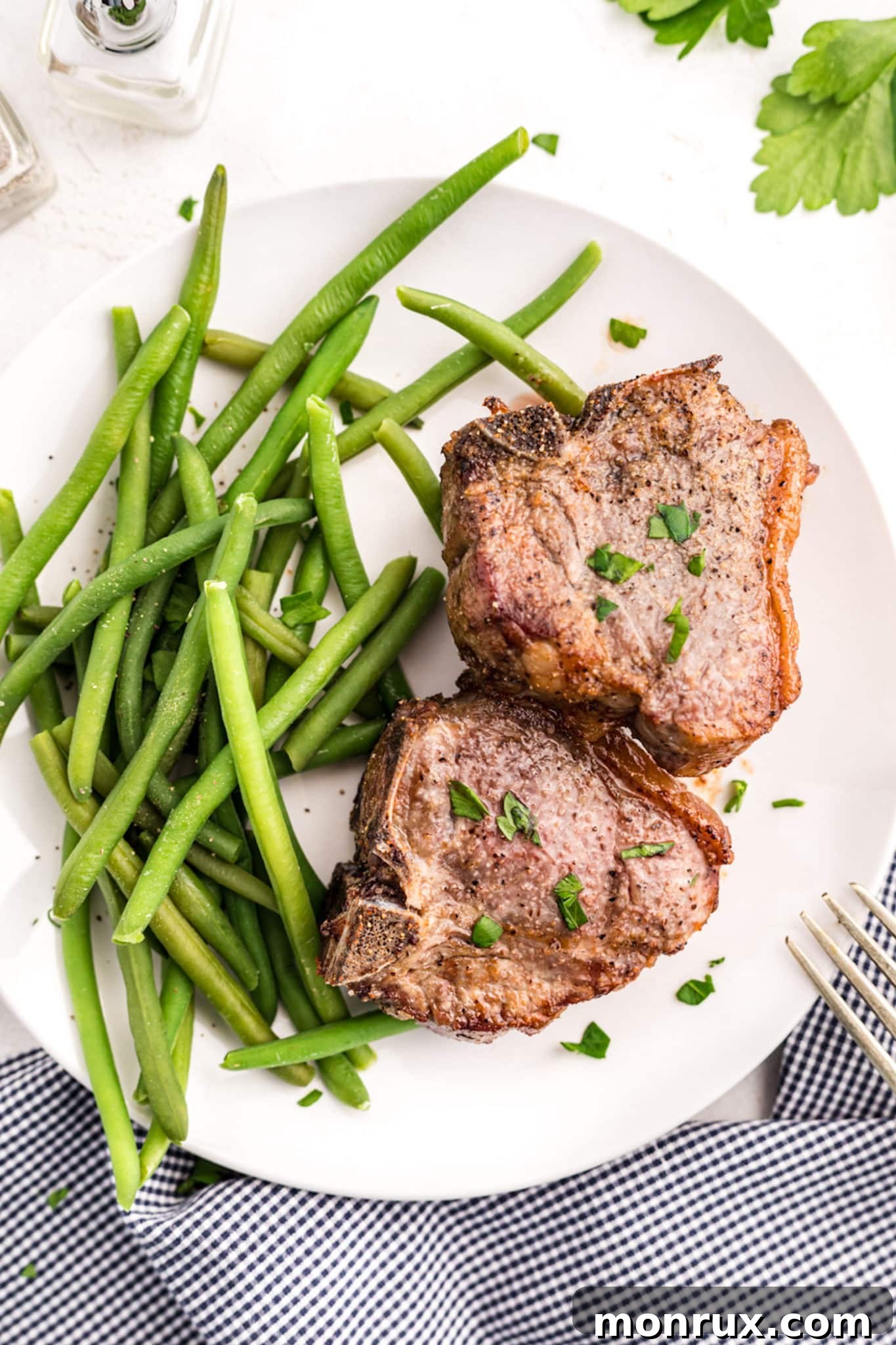 Cooked lamb chops on a white platter with cooked green beans.