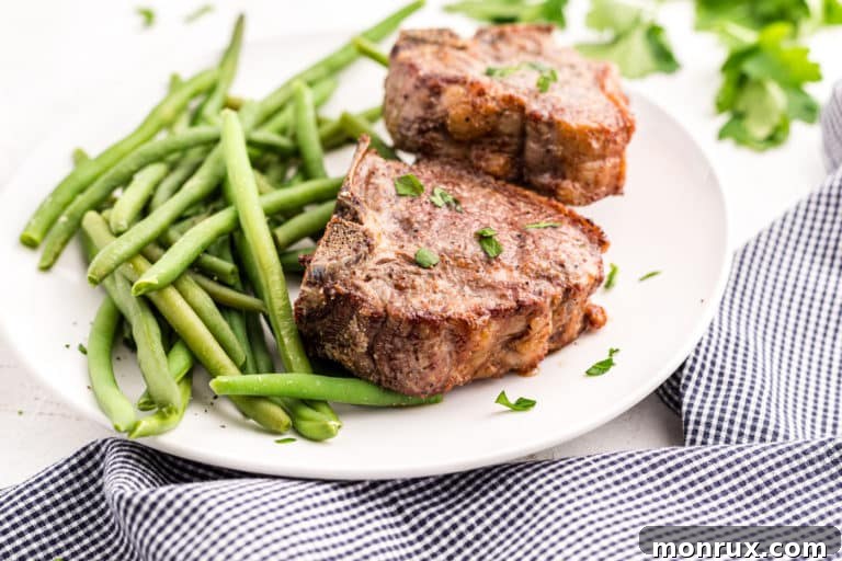 Cooked lamb chops on a white platter with cooked green beans.
